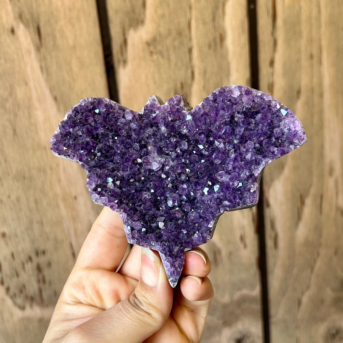 Hand holding a purple crystal against a wooden background