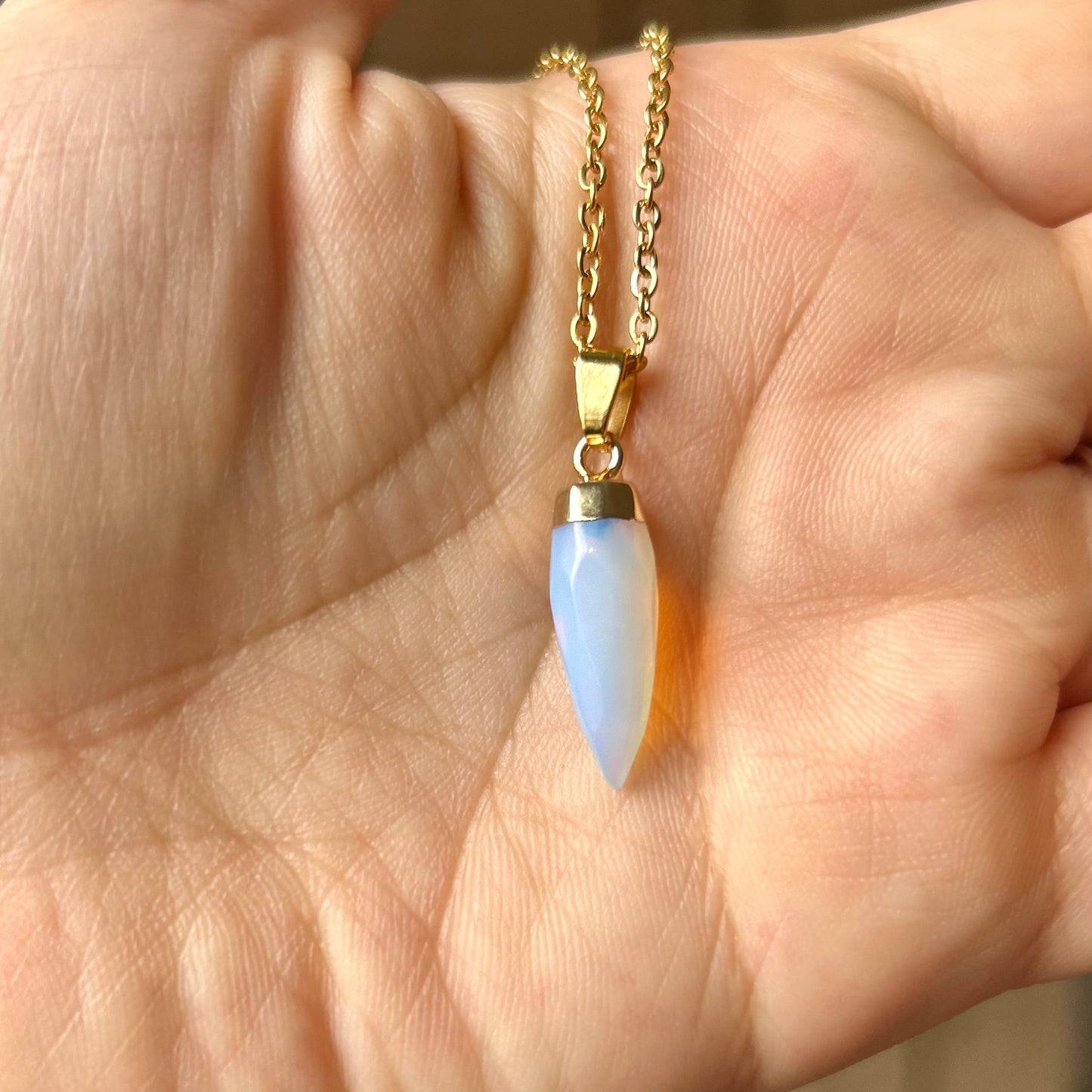 Hand holding a gold necklace with a blue pendant against a blurred background