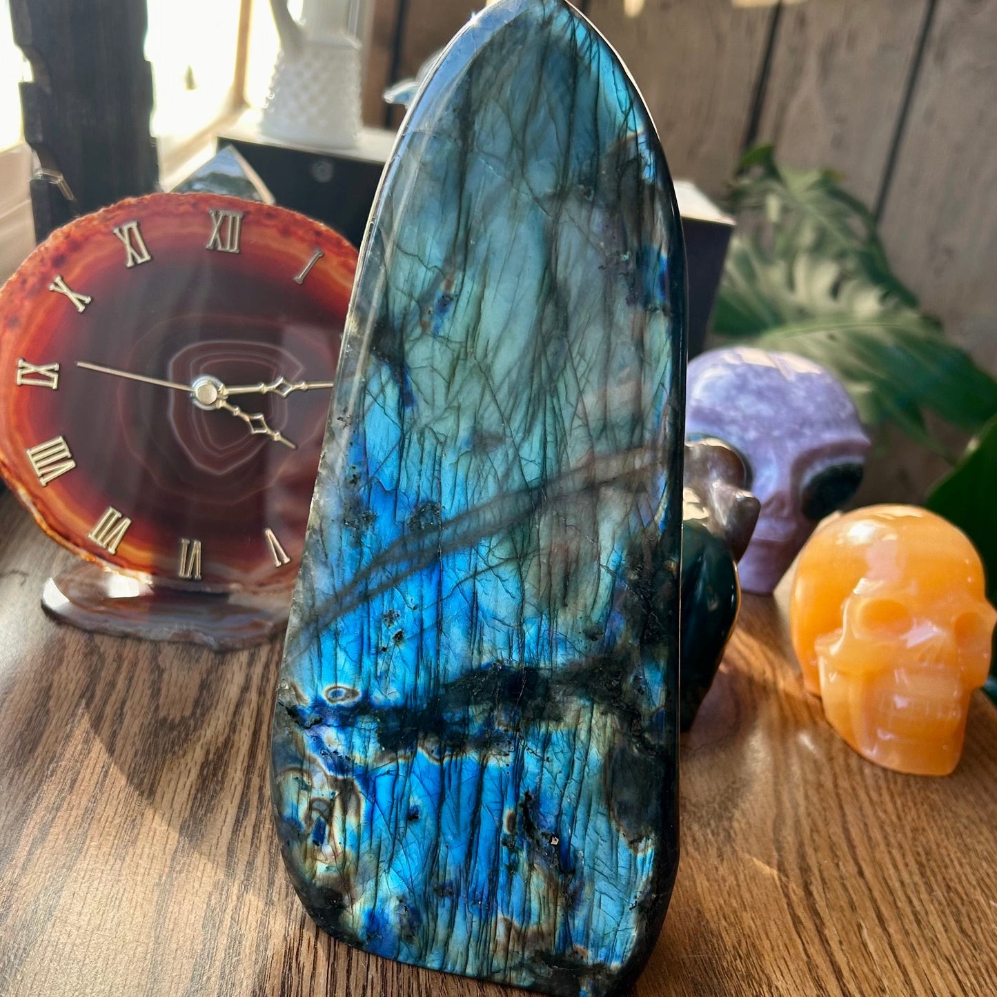 Polished labradorite stone on a wooden surface with a clock and small figurine in the background.
