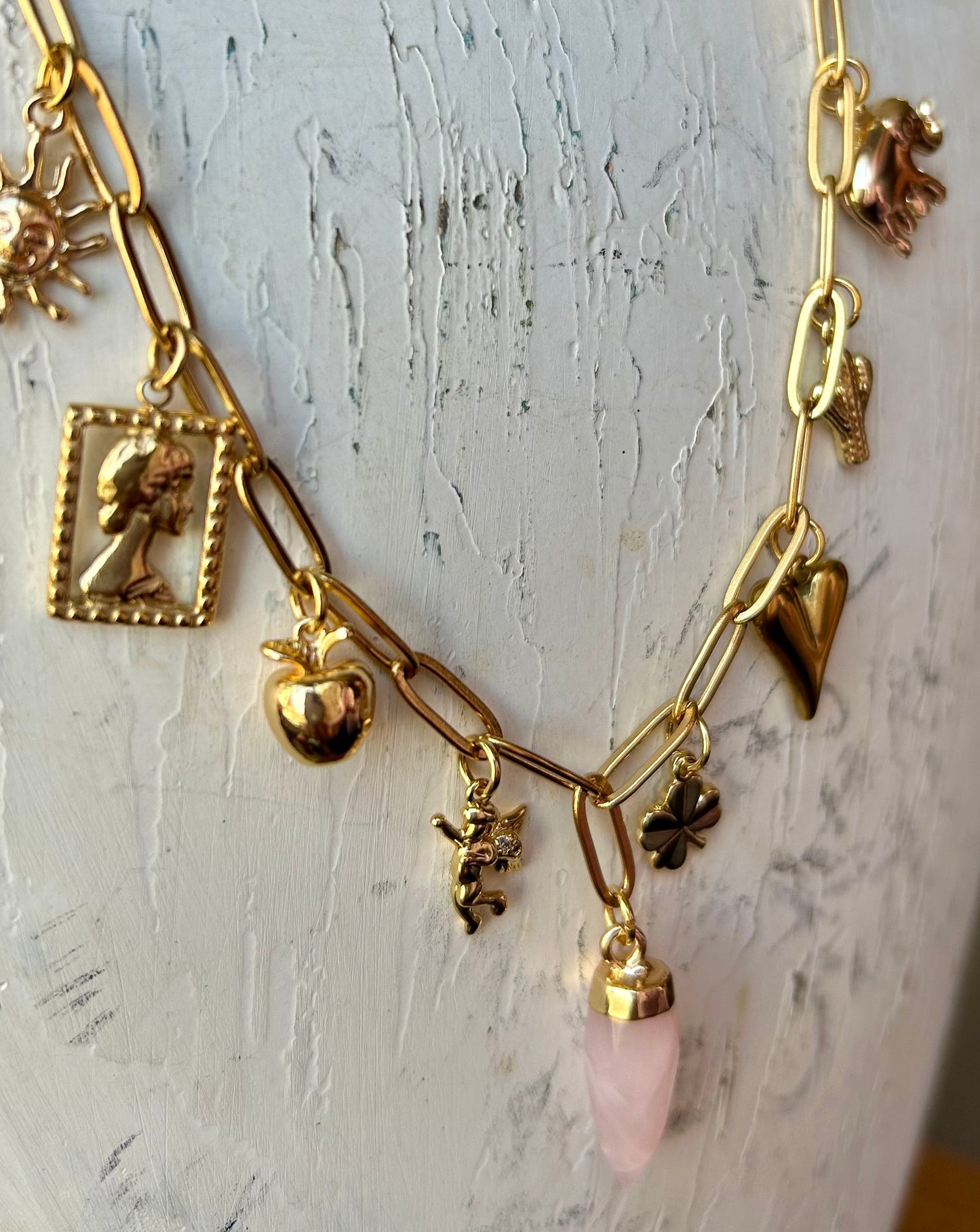 Gold necklace with various charms on a mannequin against a white background