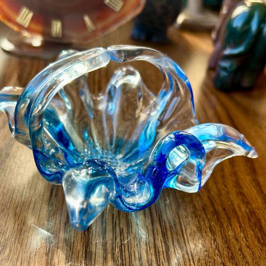 Blue glass sculpture on a wooden surface with a clock in the background