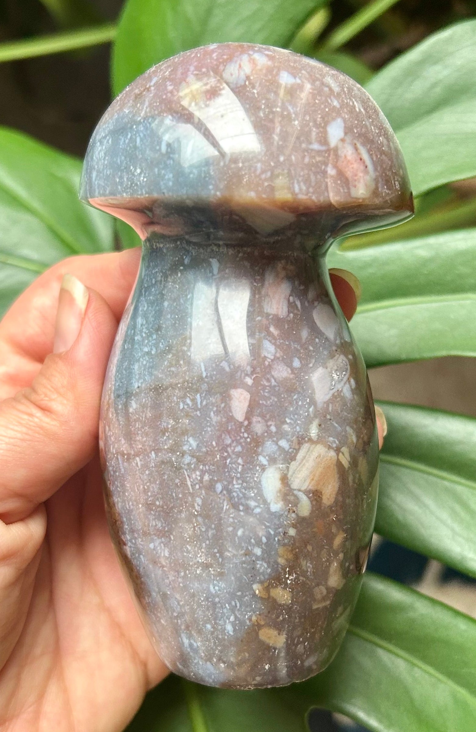 Marble-textured object held by a hand with green leaves in the background