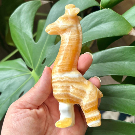 Hand holding a small giraffe figurine in front of green leaves