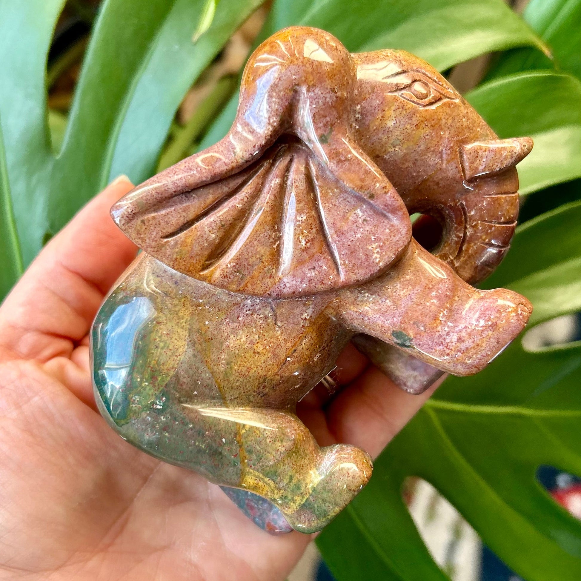 Hand holding a small brown stone sculpture against a green leafy background