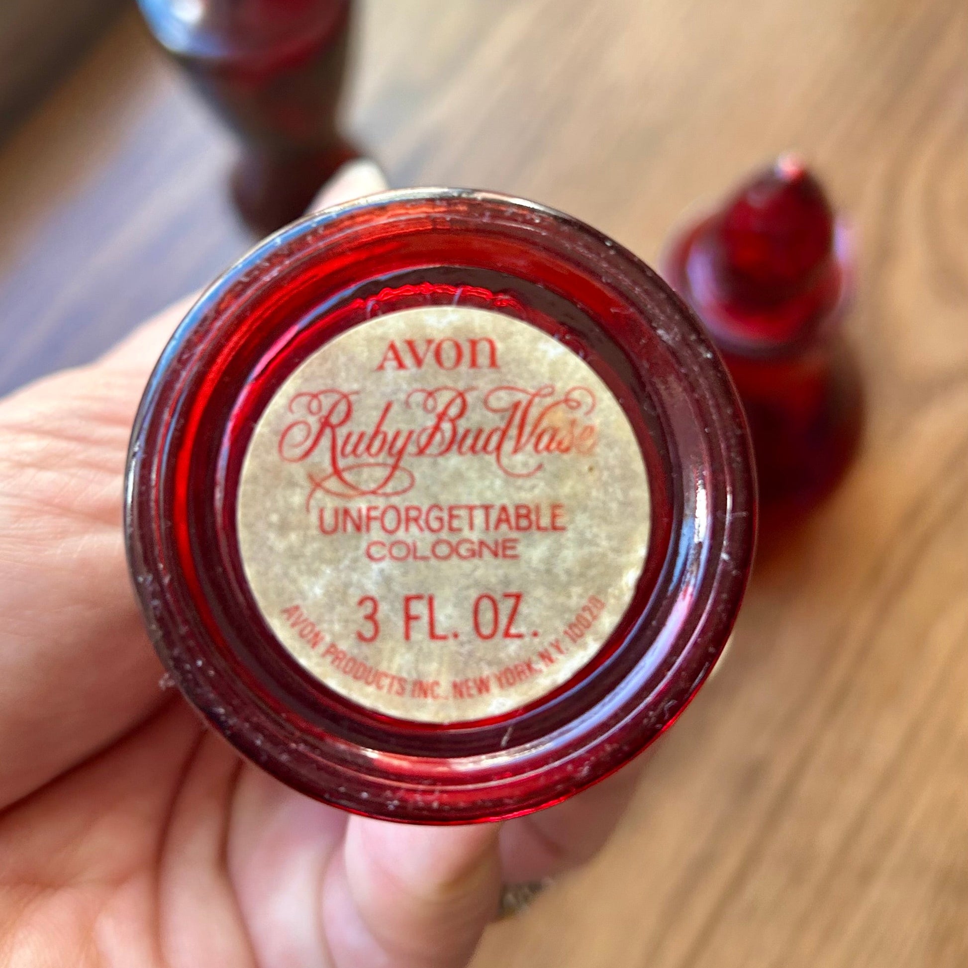 Red bottle cap of Avon Ruby Red Unforgettable Cologne on a wooden surface