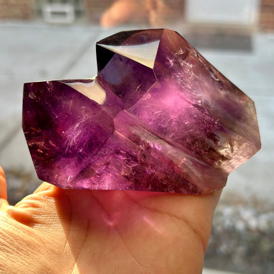 Amethyst crystal held in a hand with a blurred outdoor background