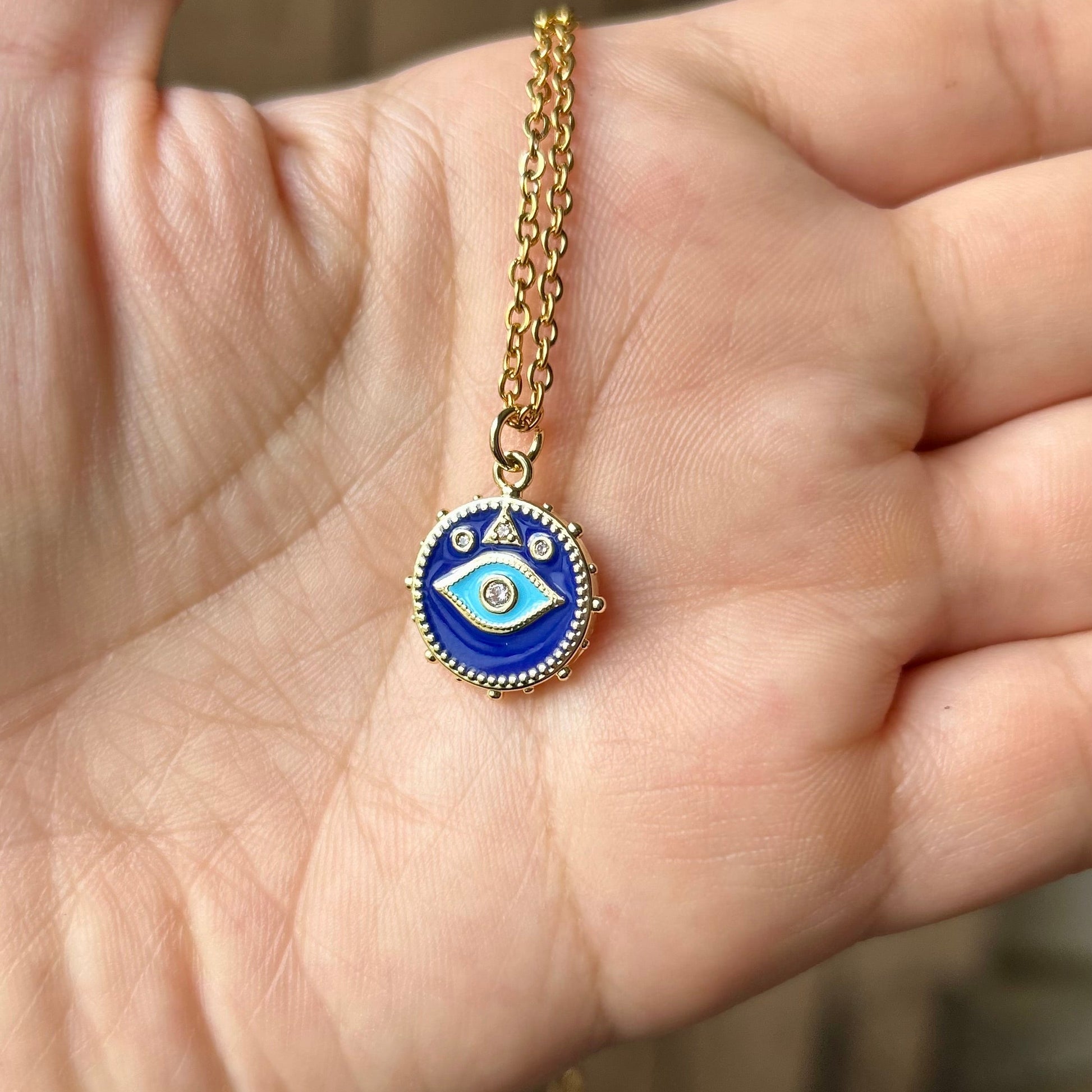 Hand holding a gold necklace with an eye-shaped pendant
