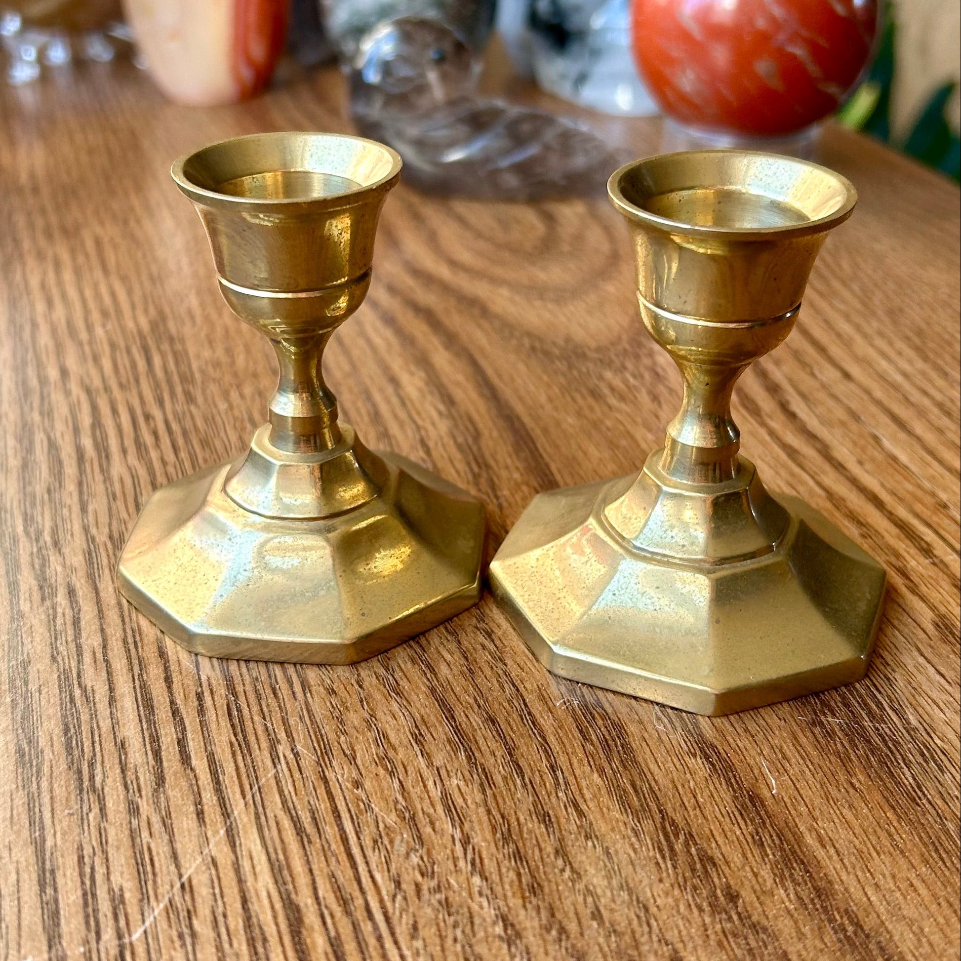Two brass candle holders on a wooden surface with decorative stones in the background.