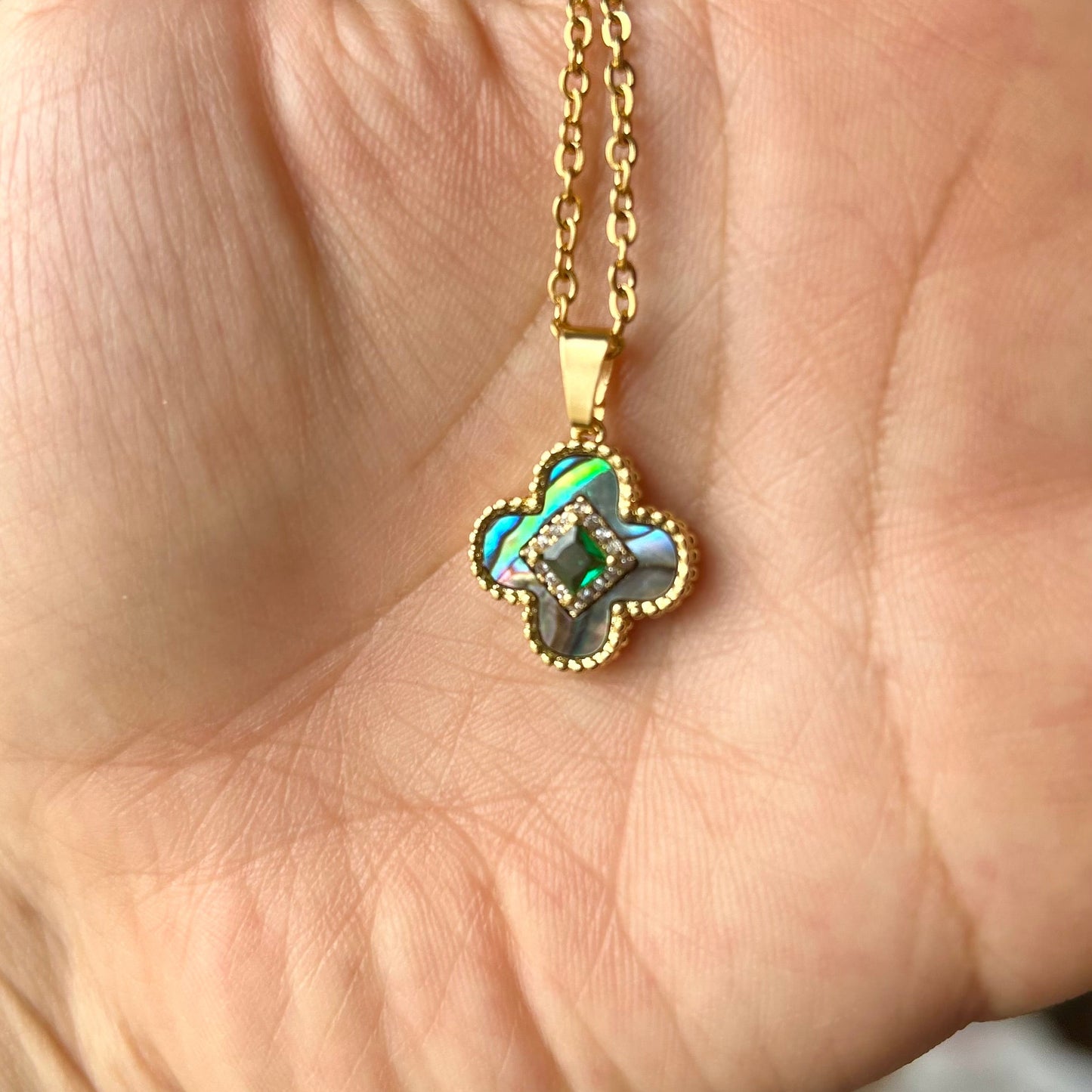 Gold necklace with a clover-shaped pendant held in a hand.