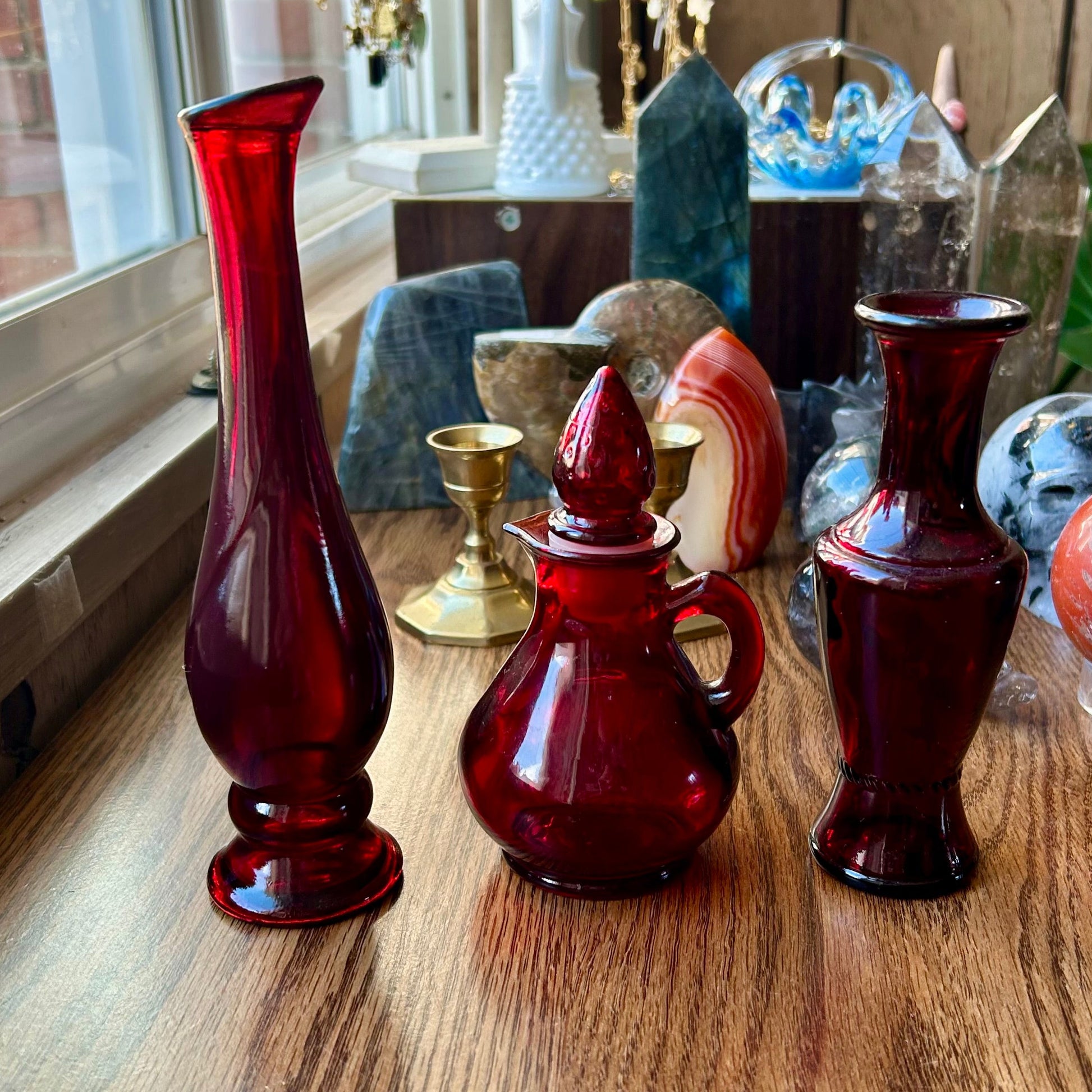 Collection of red glass vases on a wooden surface with jewelry in the background.