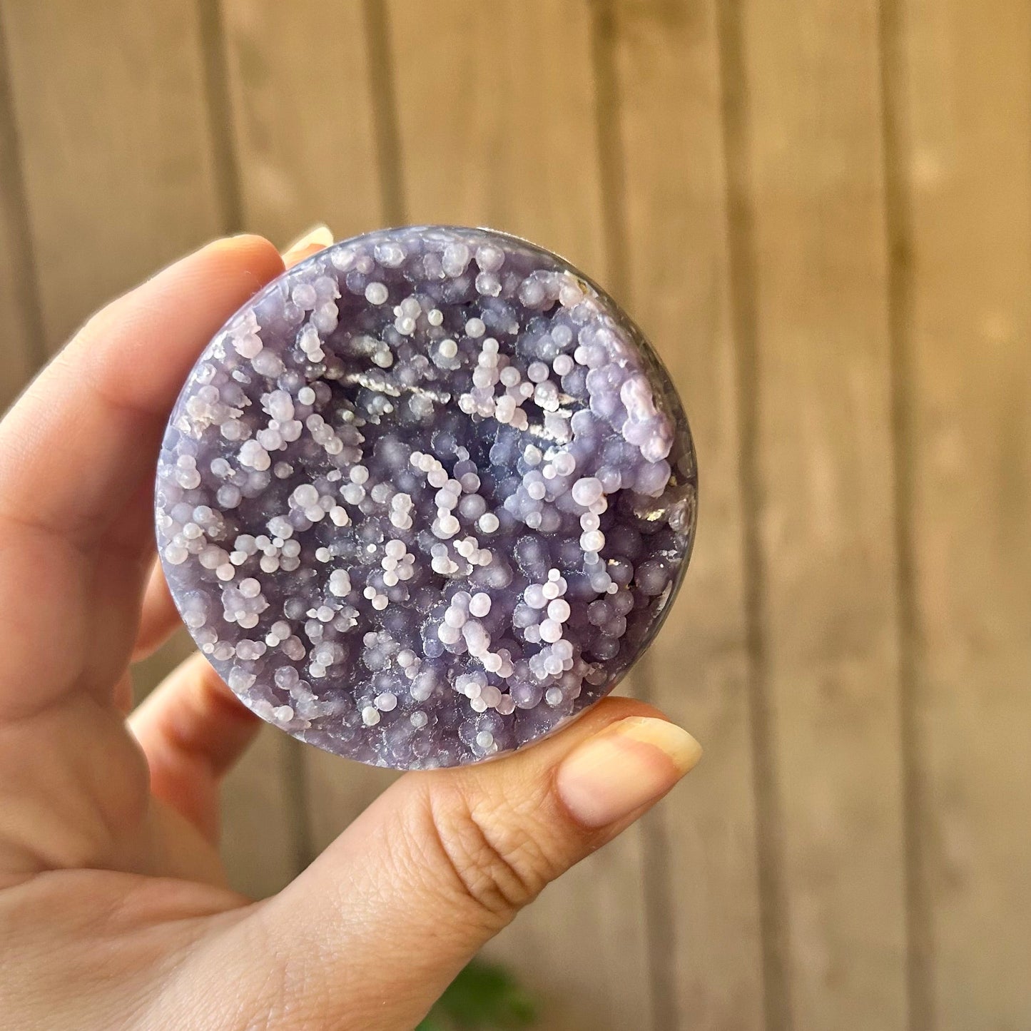 Hand holding a round, purple crystal-like object against a wooden background