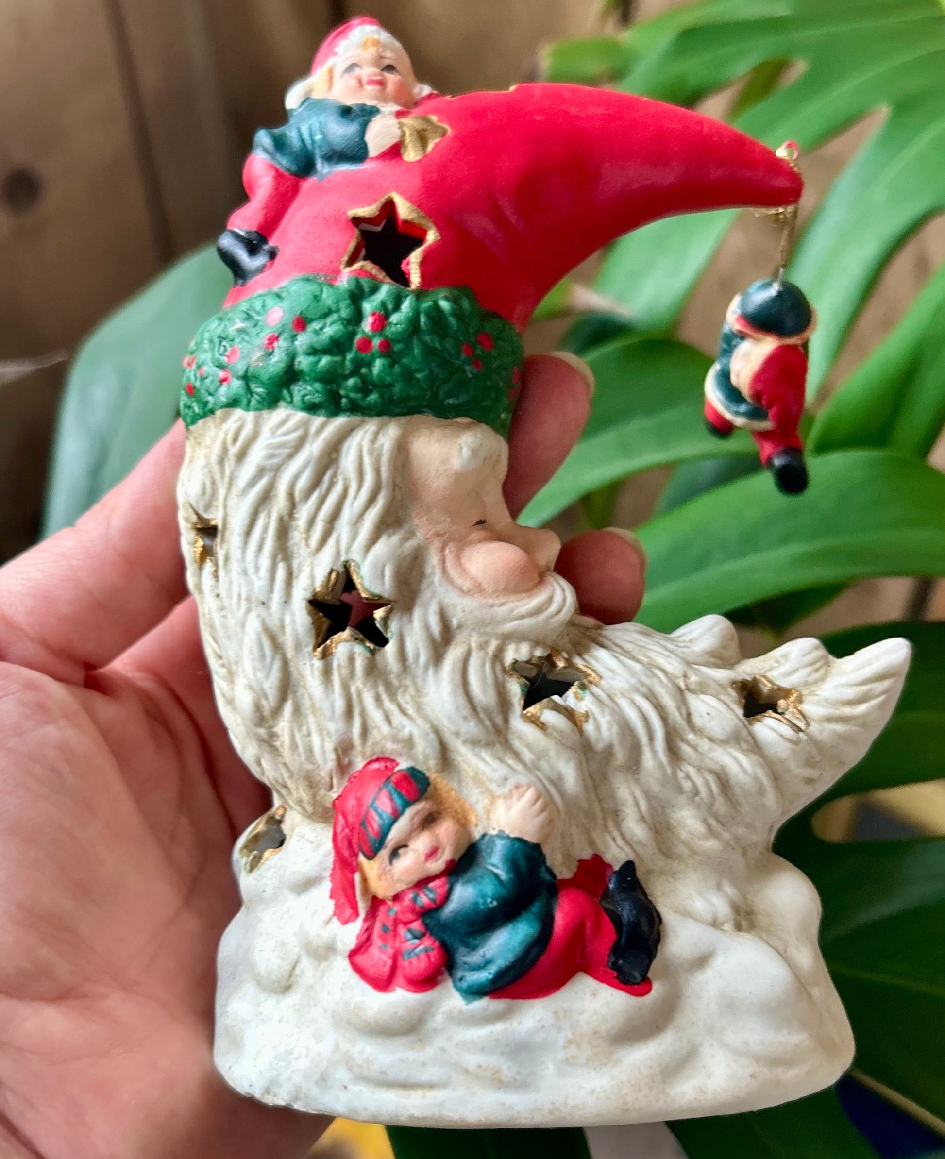 Decorative gnome figurine held in a hand with plants in the background