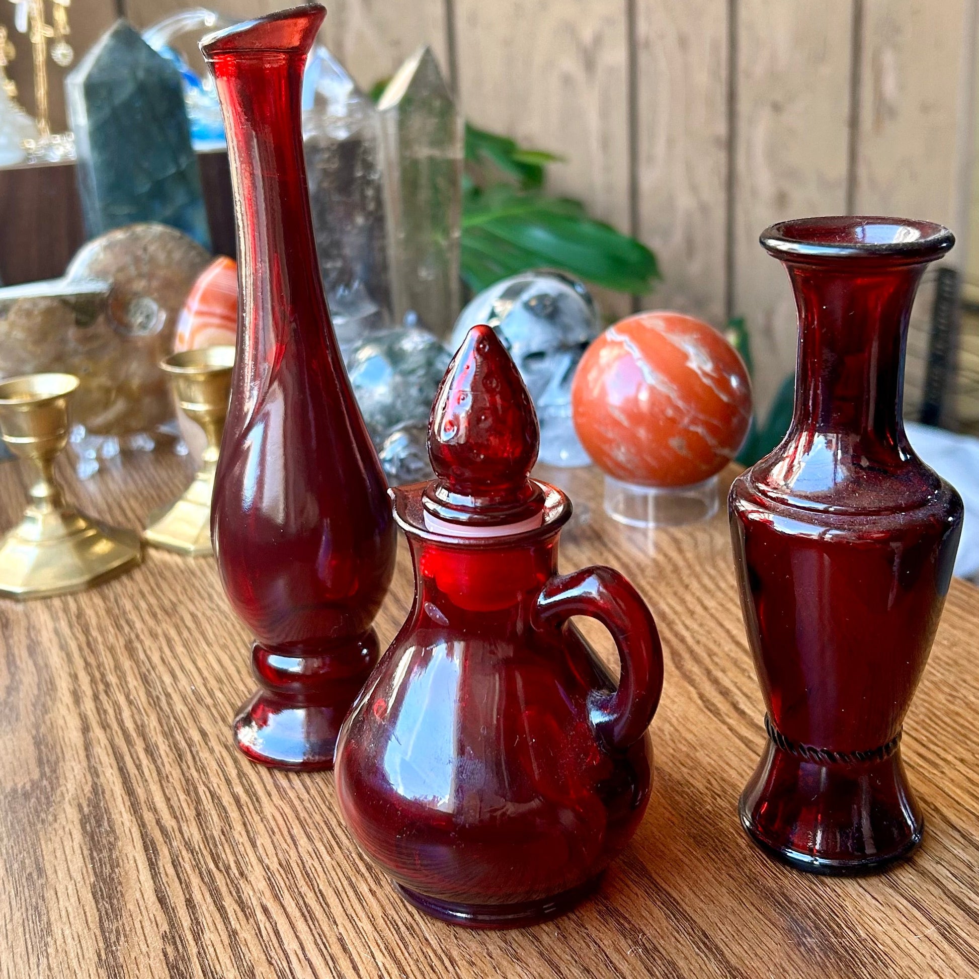 Three red glass bottles on a wooden surface with a wooden panel background