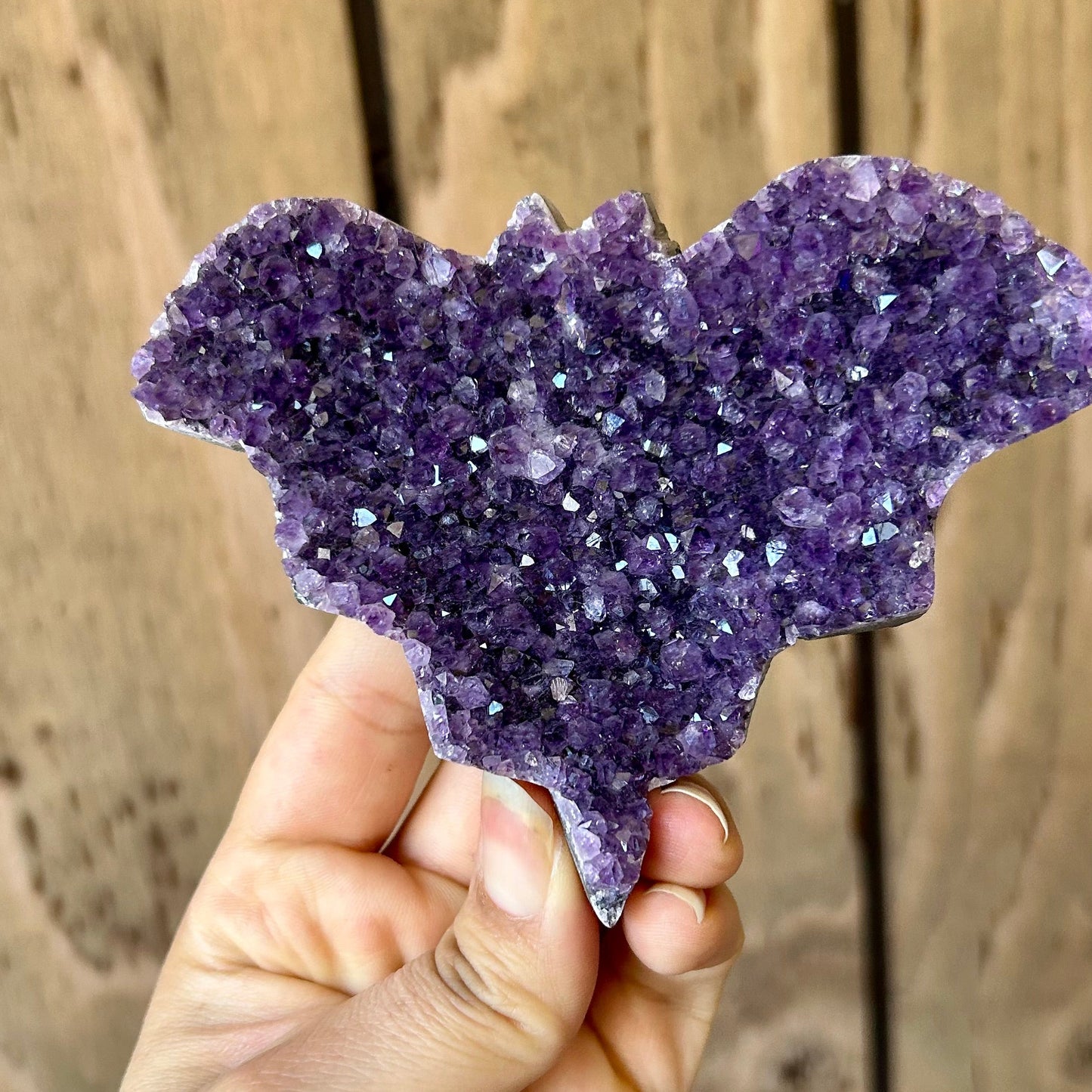 Hand holding a purple crystal formation against a wooden background