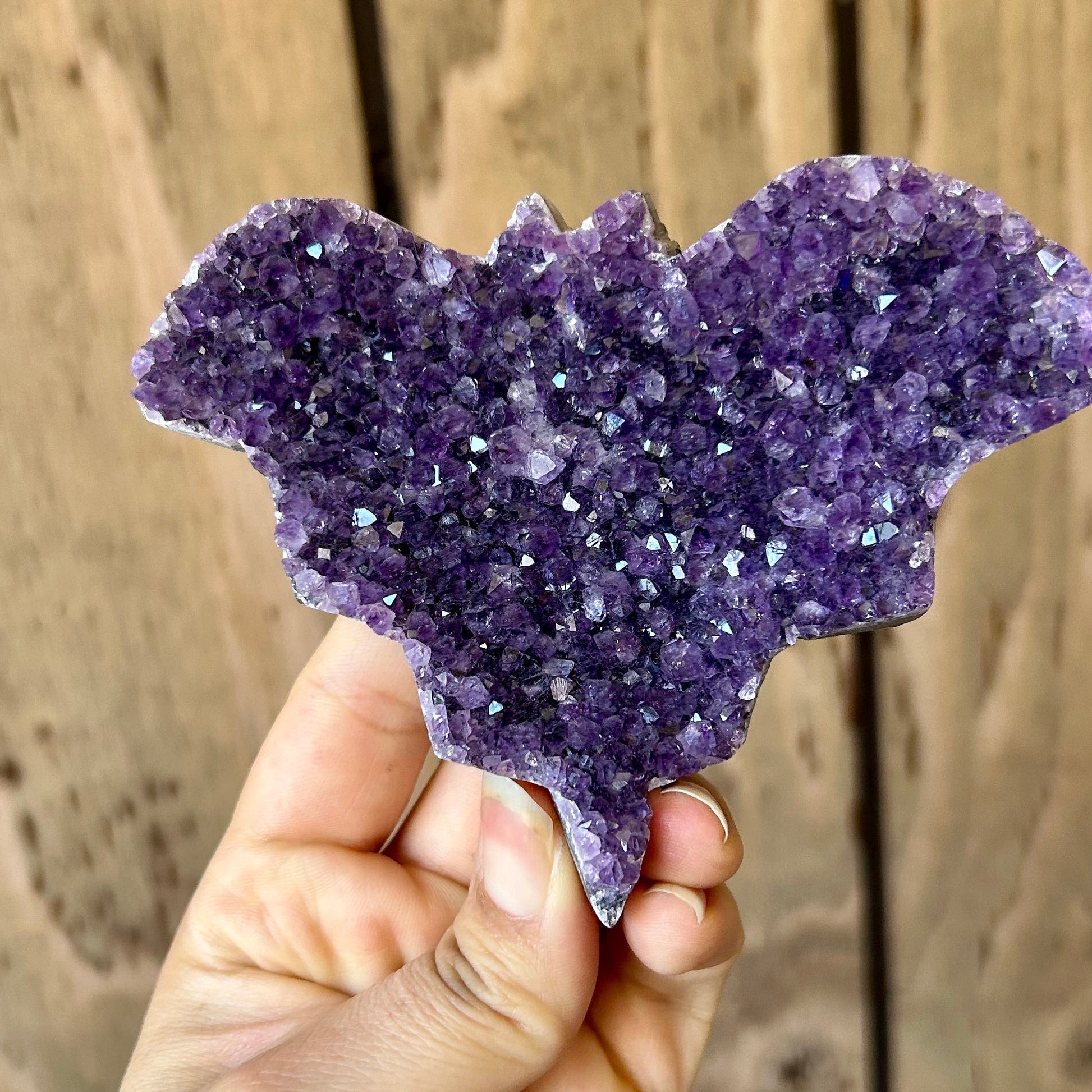 Hand holding a purple crystal formation against a wooden background