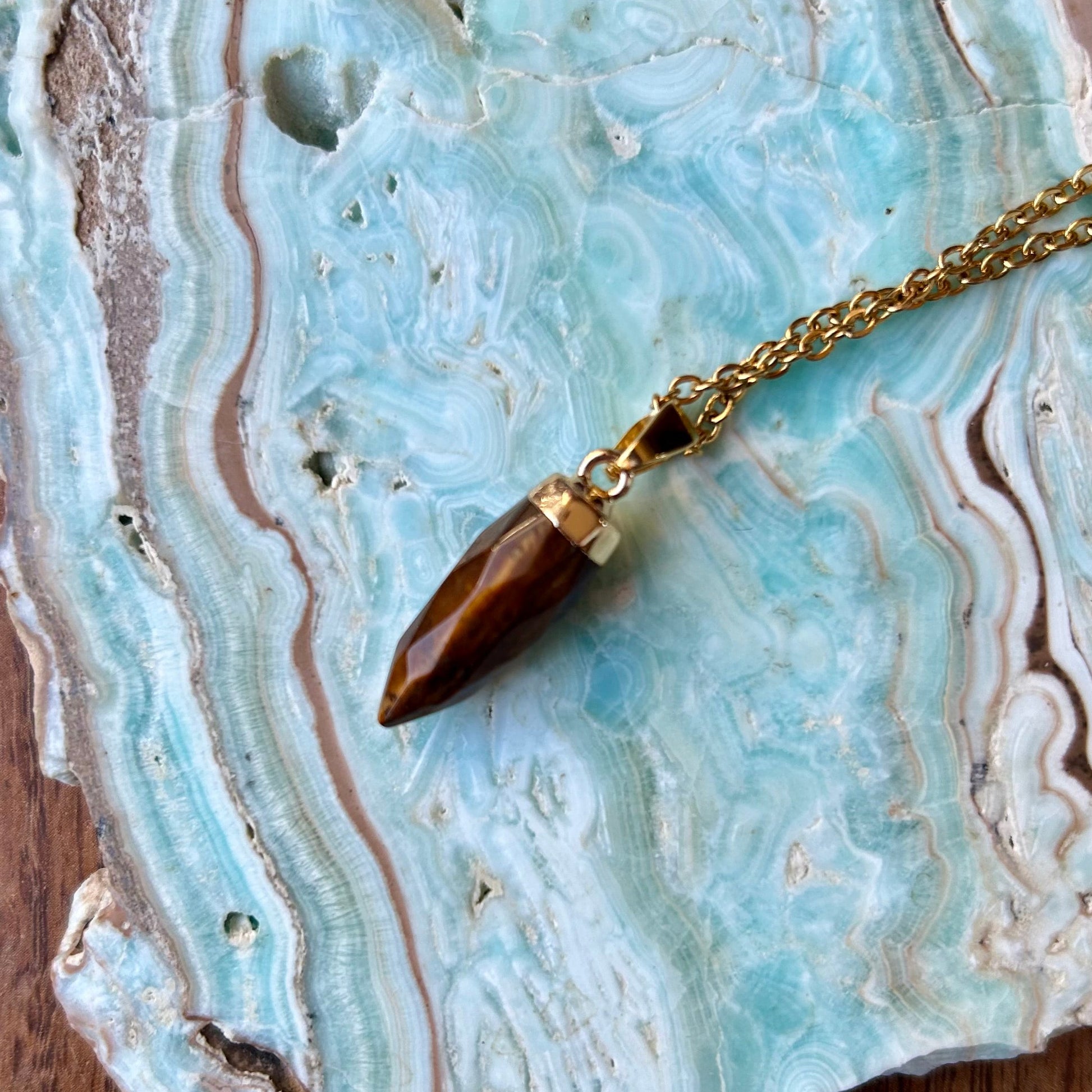 Gold necklace with a brown pendant on a textured stone surface