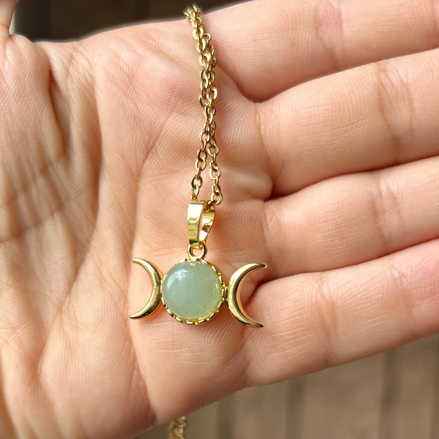Hand holding a gold necklace with a green pendant against a blurred background