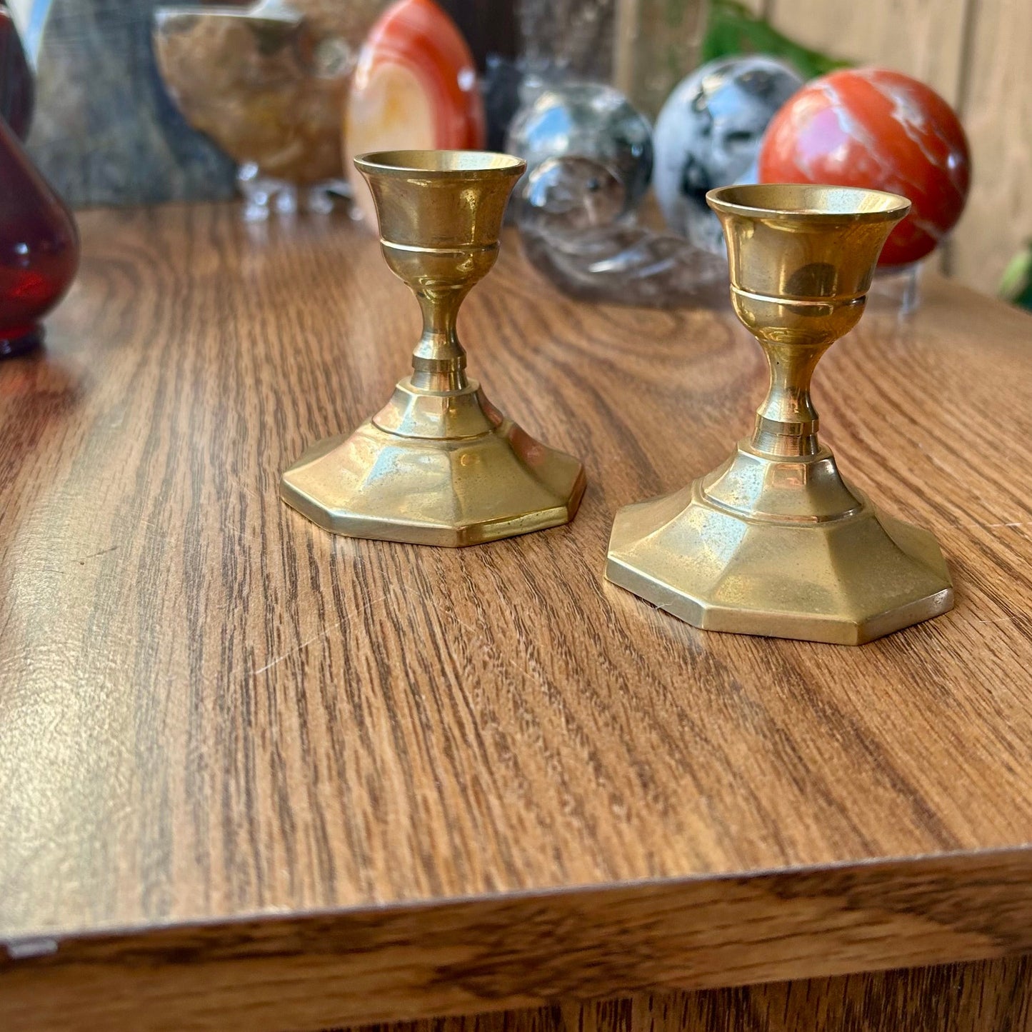 Two gold candle holders on a wooden surface with decorative items in the background.