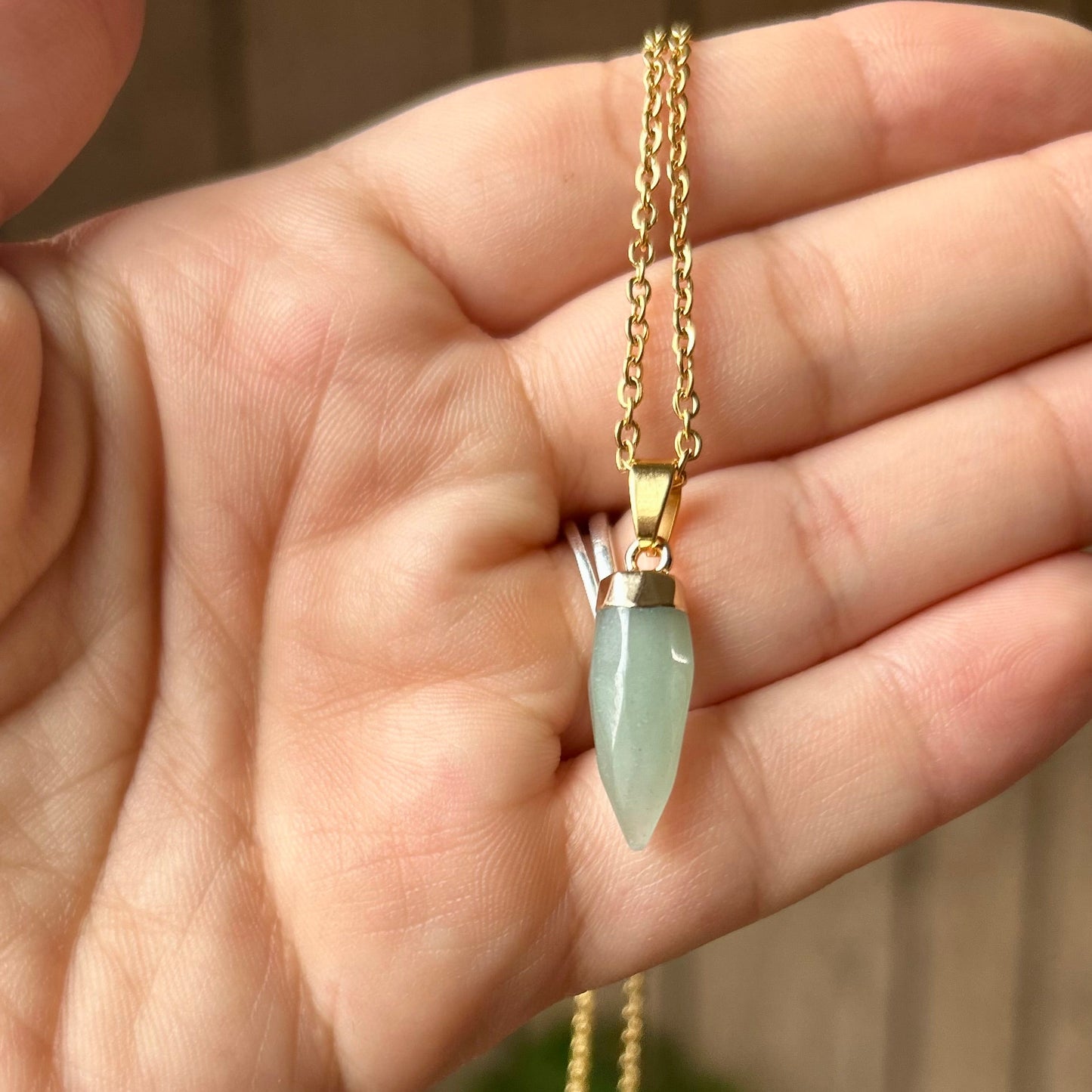 Gold necklace with a green gemstone pendant held in a hand against a blurred background