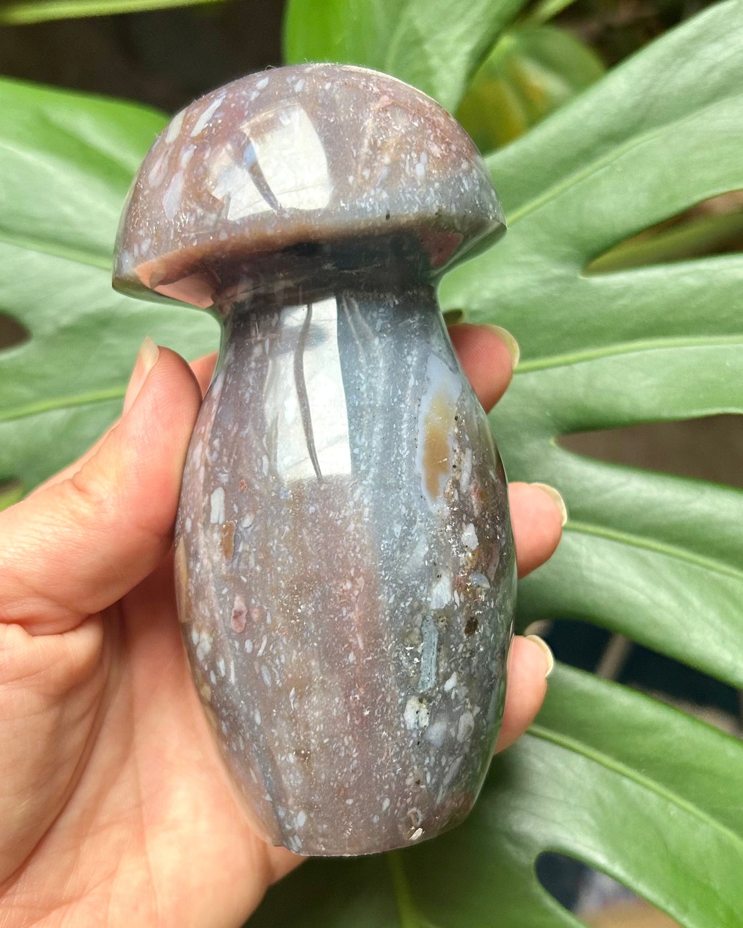Hand holding a small ceramic mushroom-shaped object with green leaves in the background