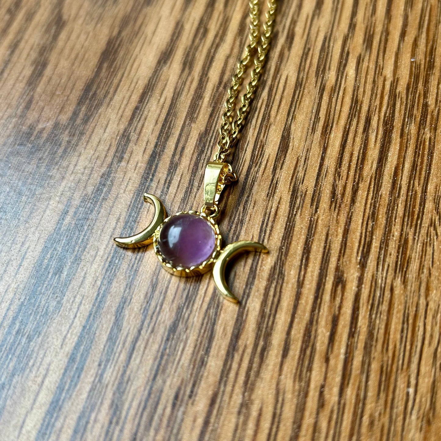 Gold necklace with a purple gemstone pendant on a wooden surface