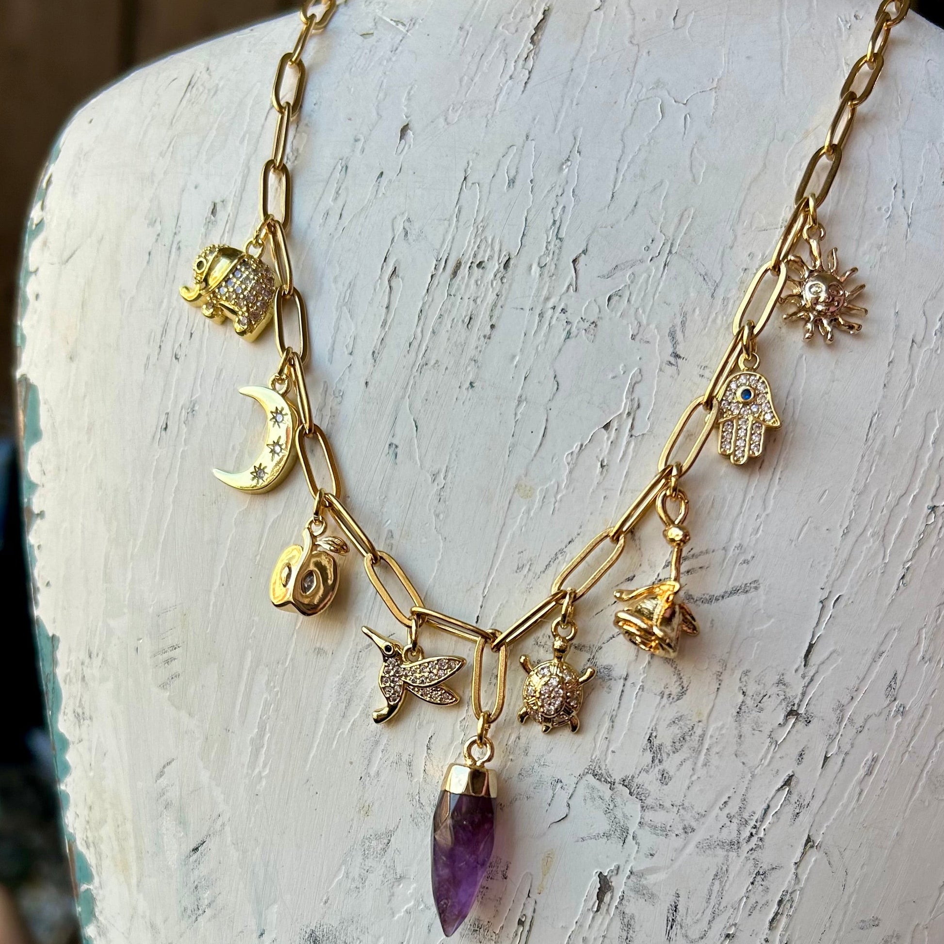 Gold necklace with amethyst pendant on a white wooden stand