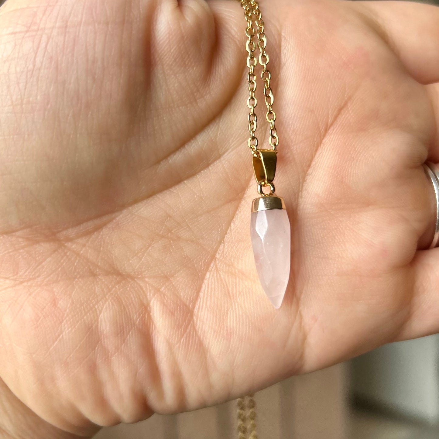 Hand holding a gold necklace with a pink pendant against a blurred background