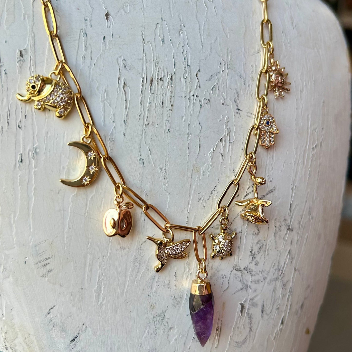 Gold necklace with various charms on a mannequin bust.