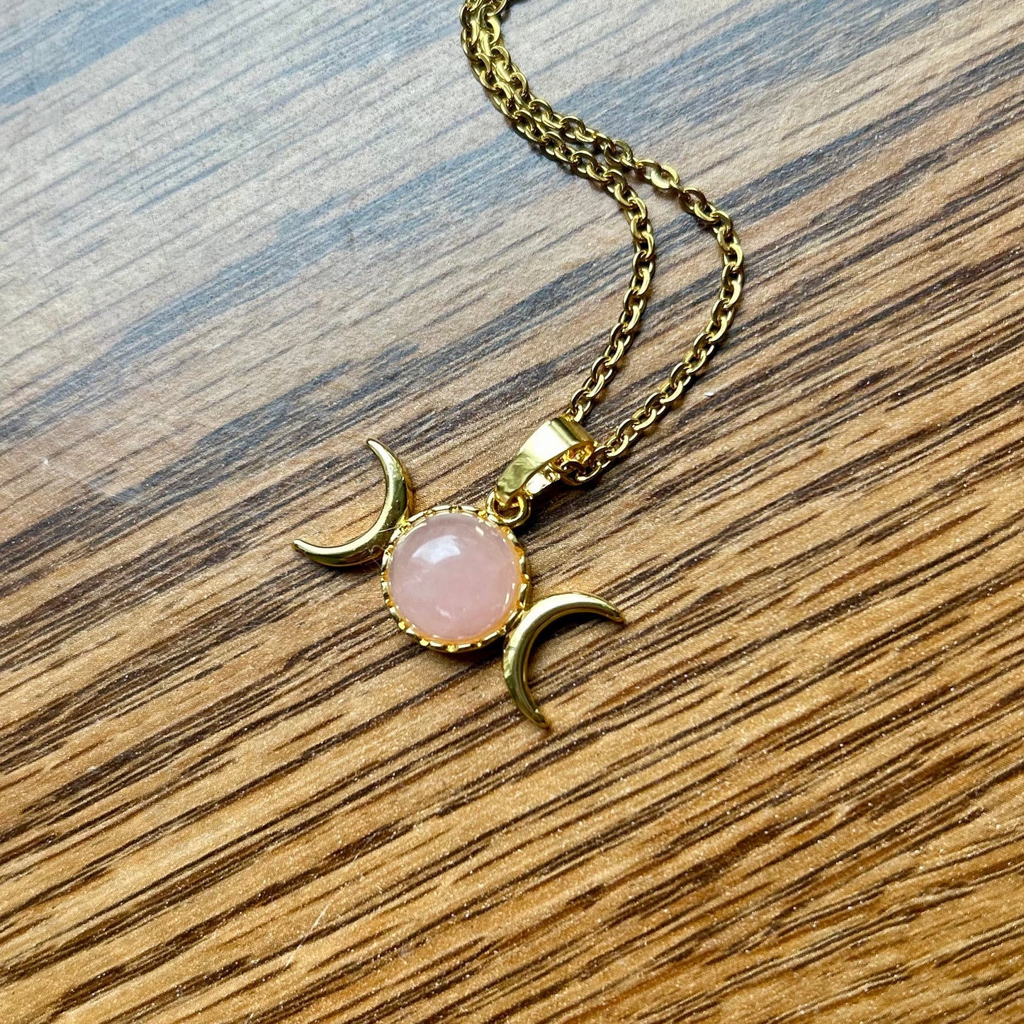 Necklace with a pink stone and gold crescent moon pendant on a wooden surface
