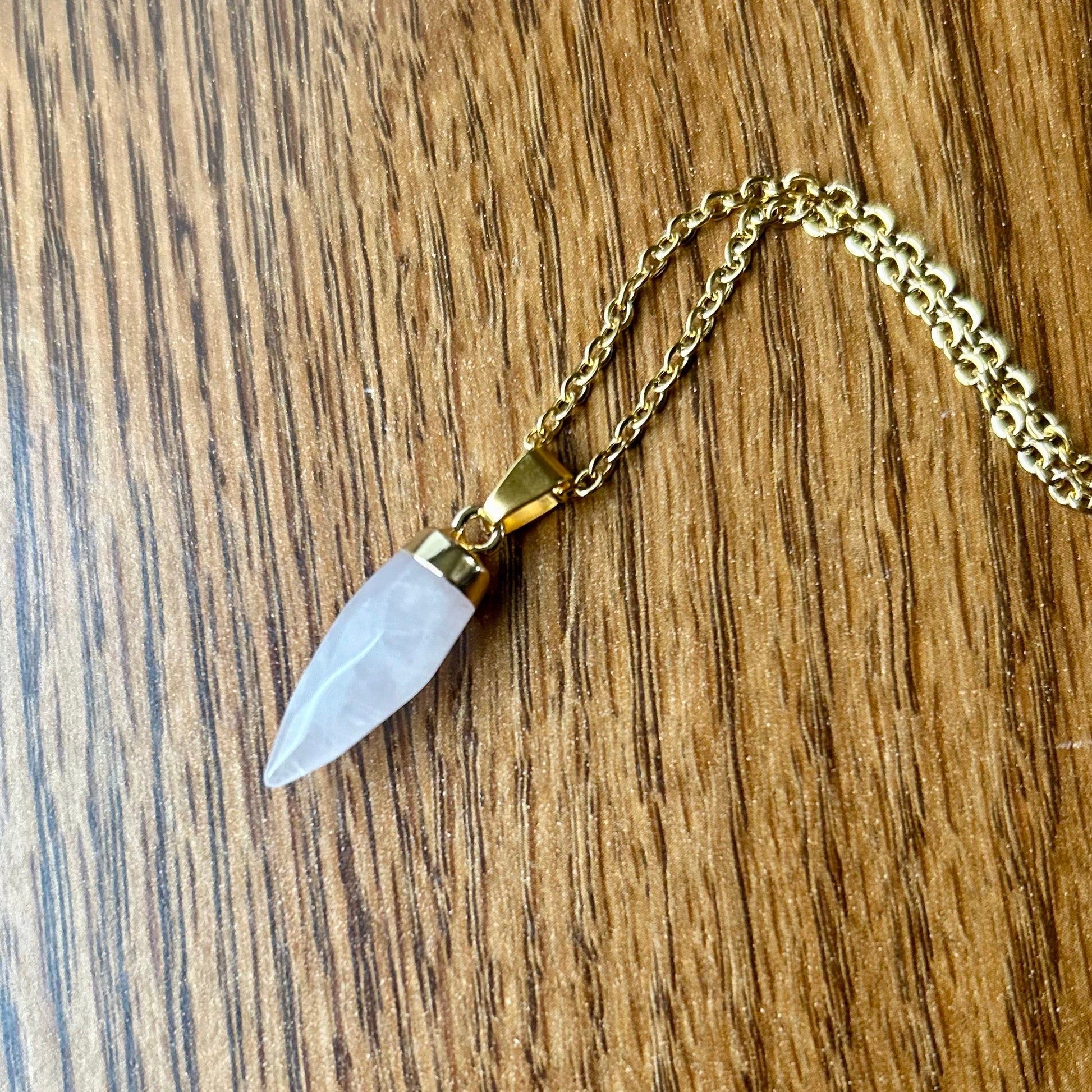 Gold necklace with a silver arrowhead pendant on a wooden surface