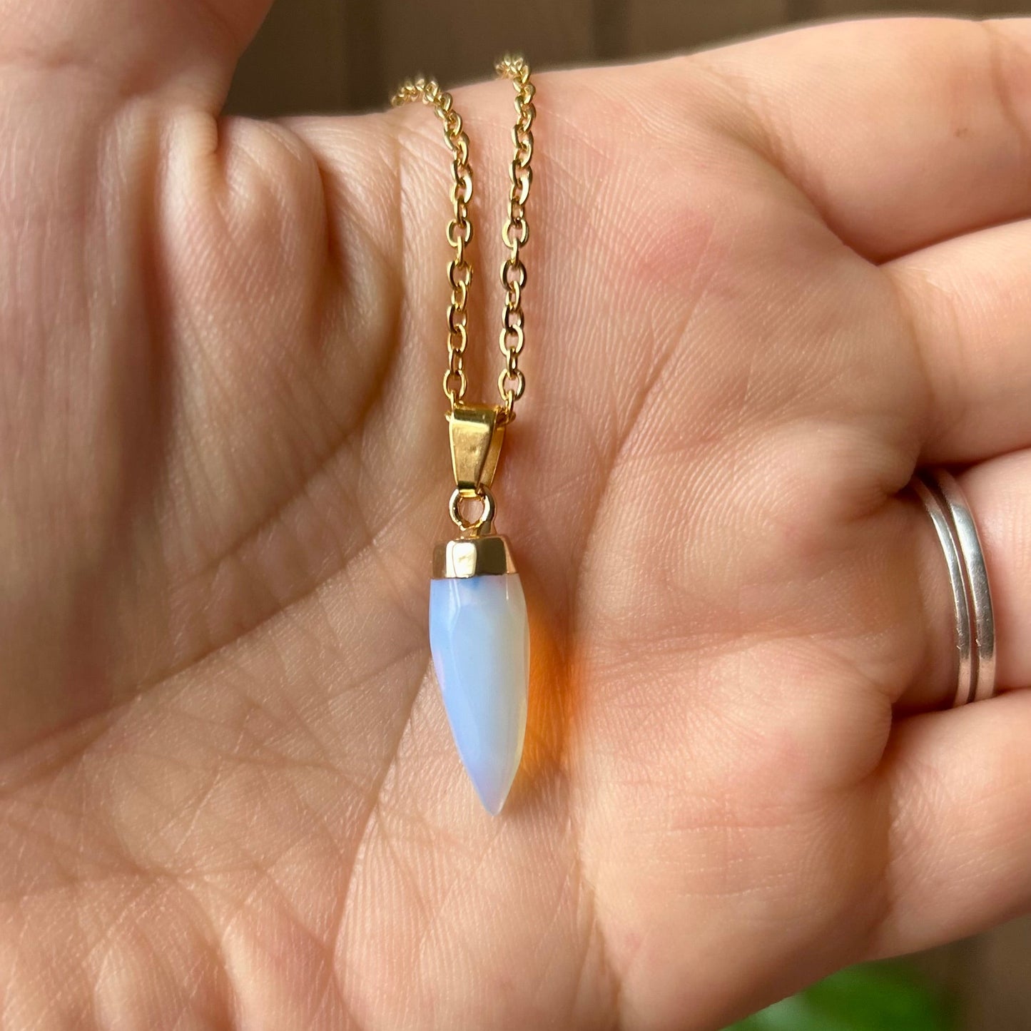 Hand holding a gold necklace with a blue pendant against a blurred background