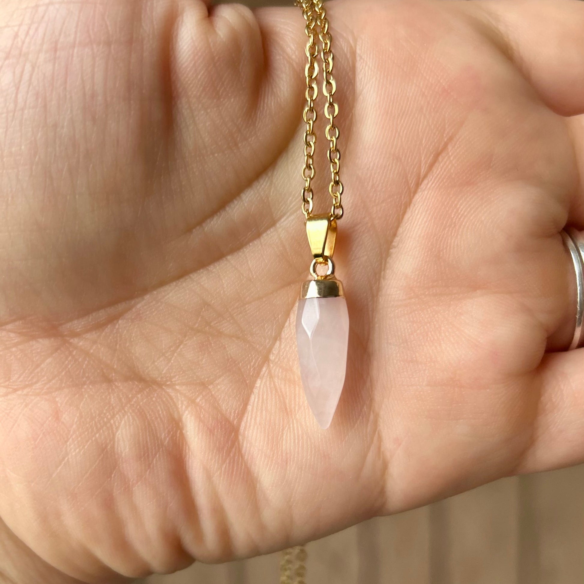 Hand wearing a gold bracelet with a pink pendant against a blurred background