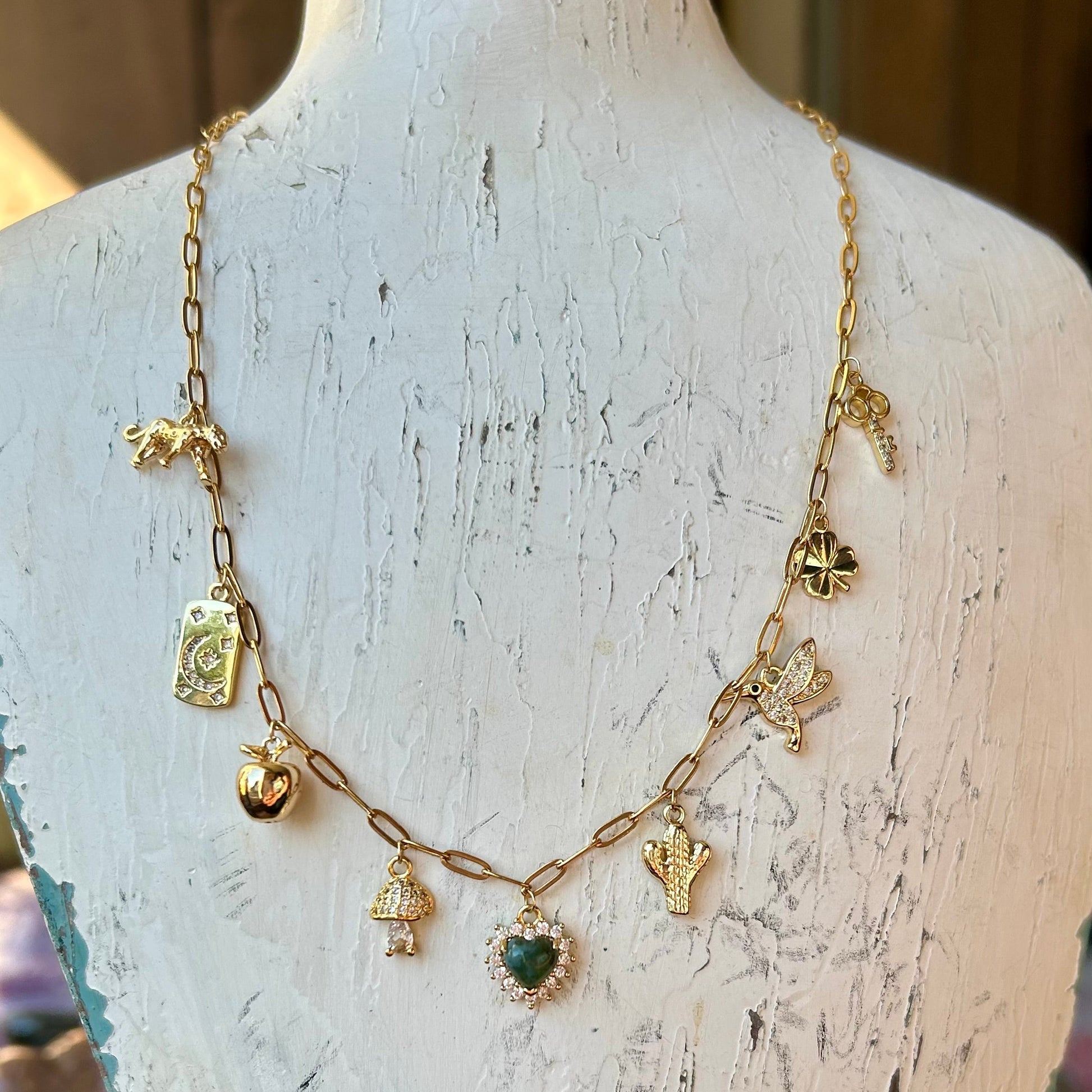 Gold necklace with various charms on a rustic wooden stand.