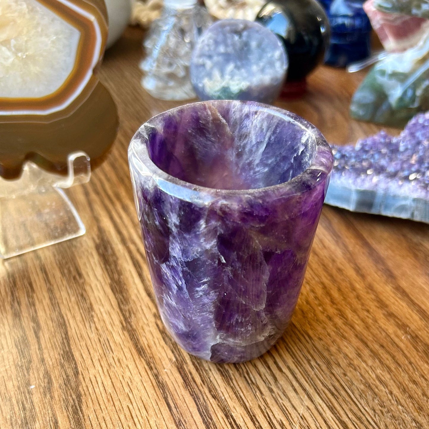Amethyst crystal shot glass on a wooden surface with other crystals in the background