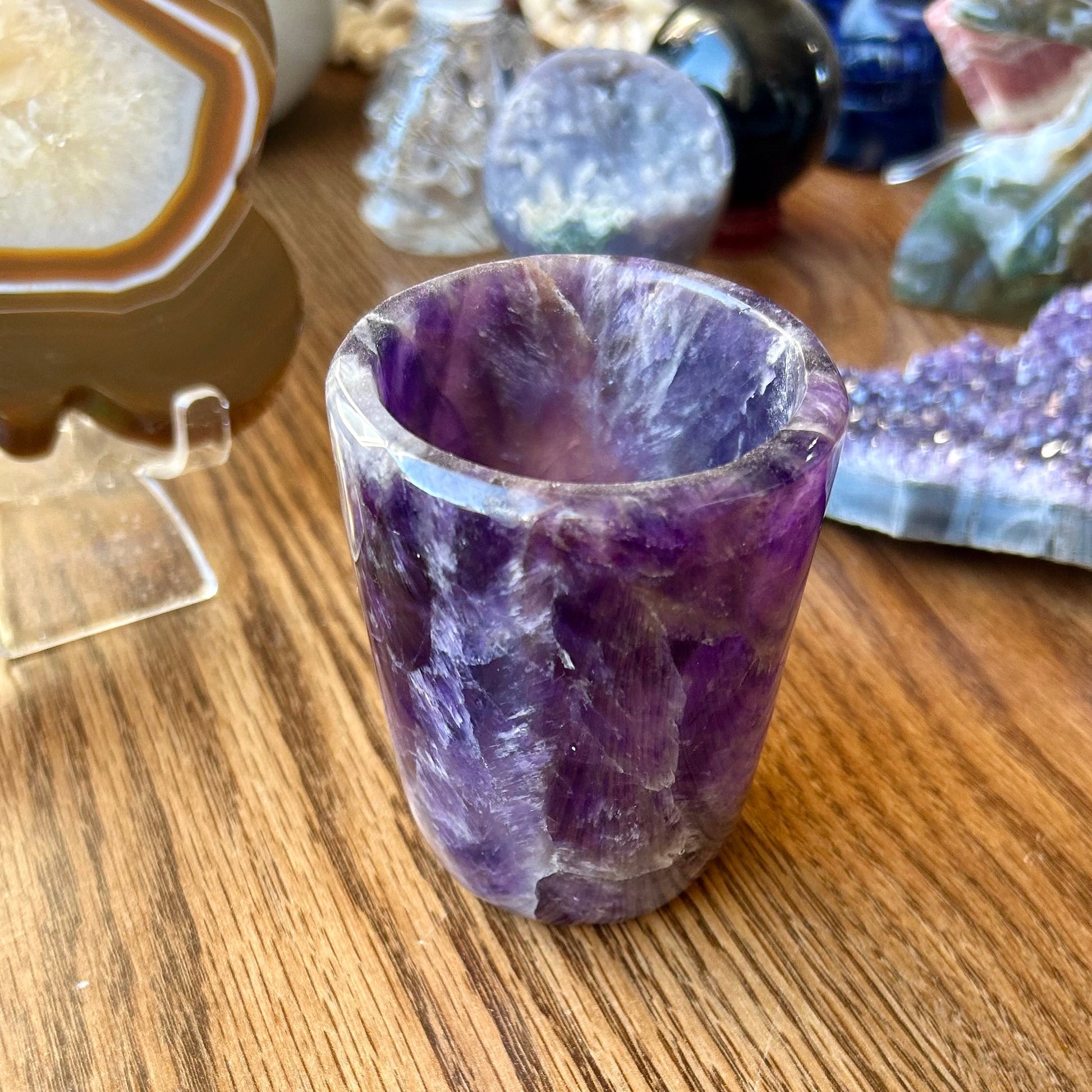 Amethyst crystal shot glass on a wooden surface with other crystals in the background