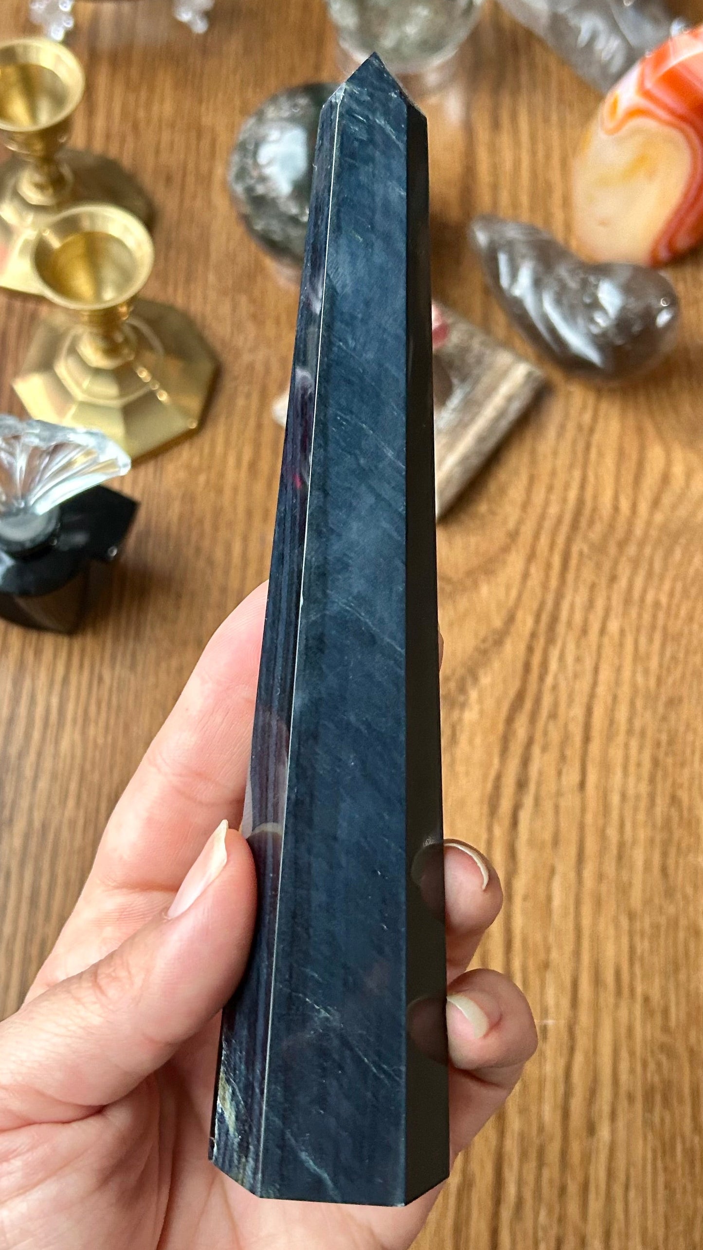 Hand holding a dark crystal on a wooden surface with various decorative items in the background
