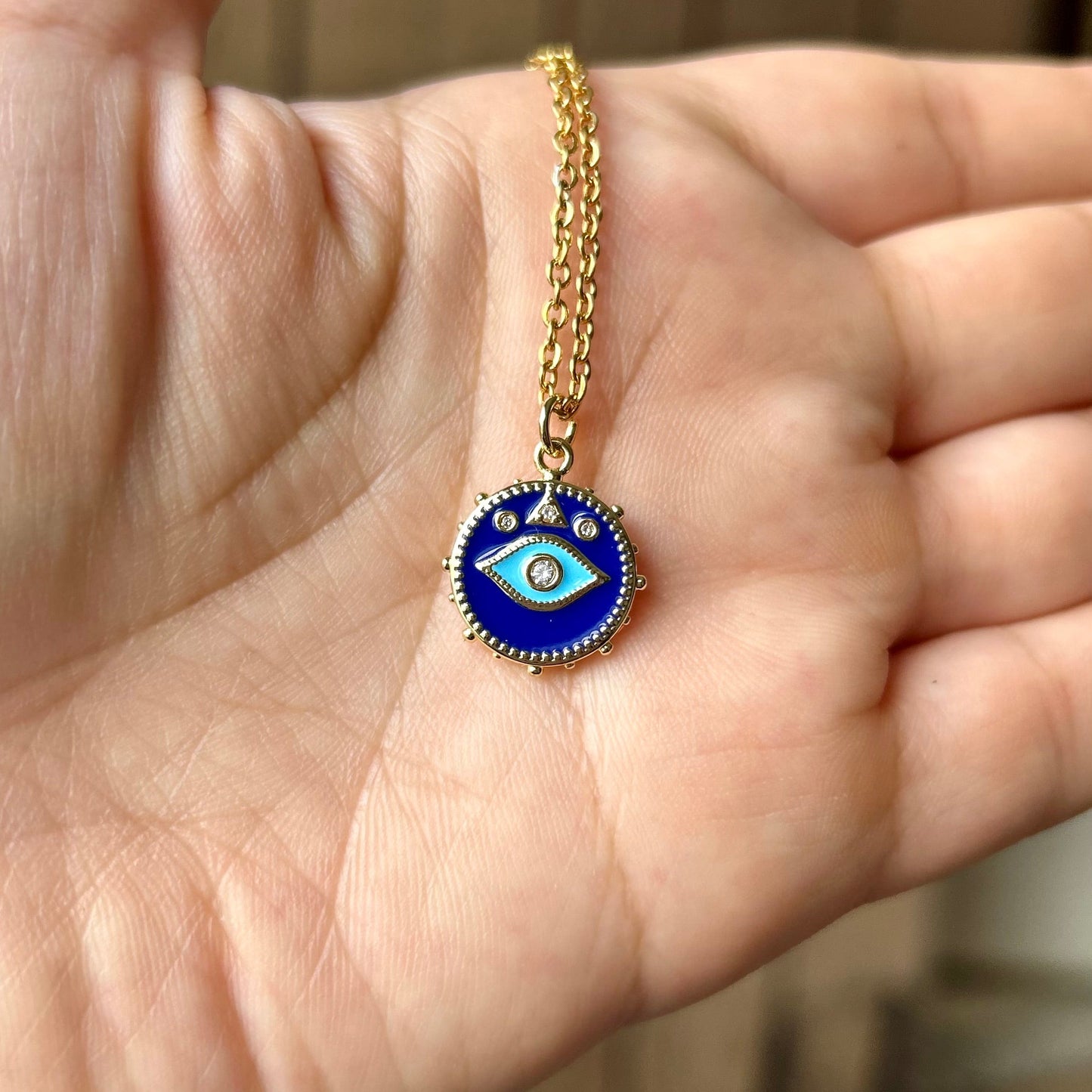 Hand holding a gold necklace with an eye-shaped pendant