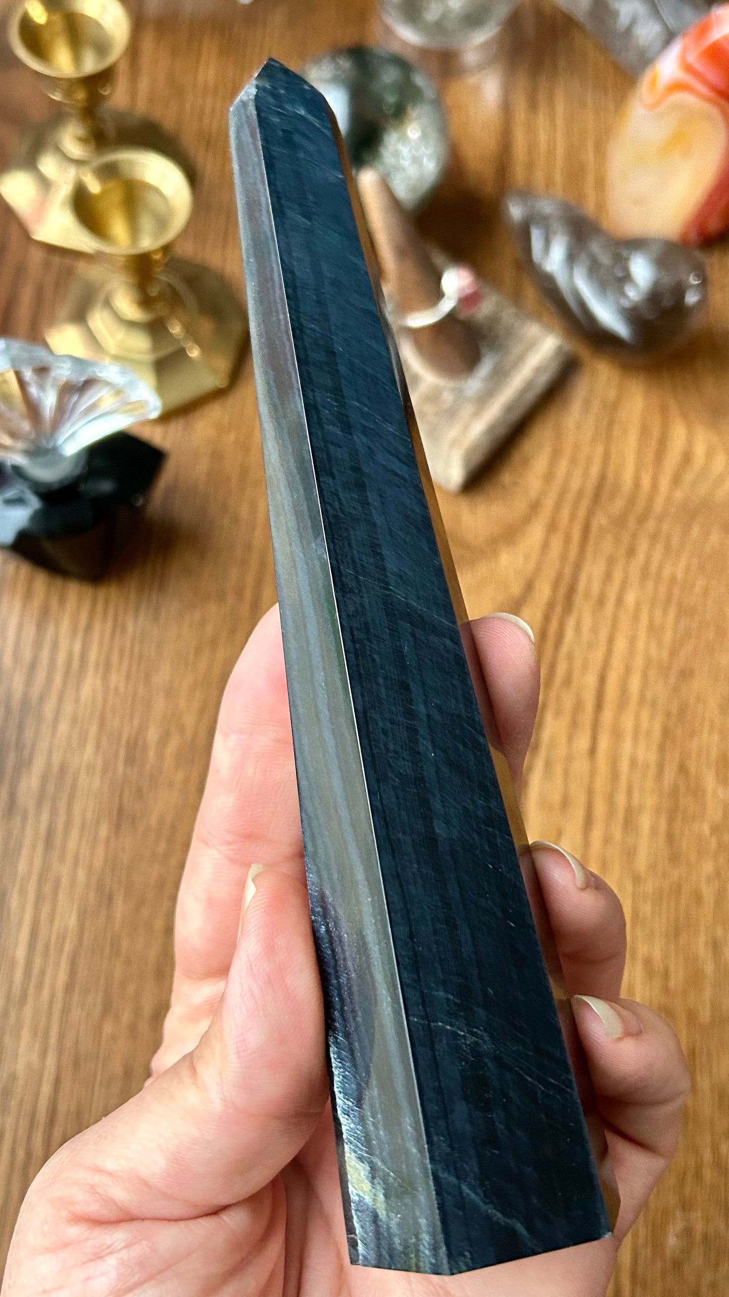 Person holding a long, dark stone with decorative items in the background on a wooden surface