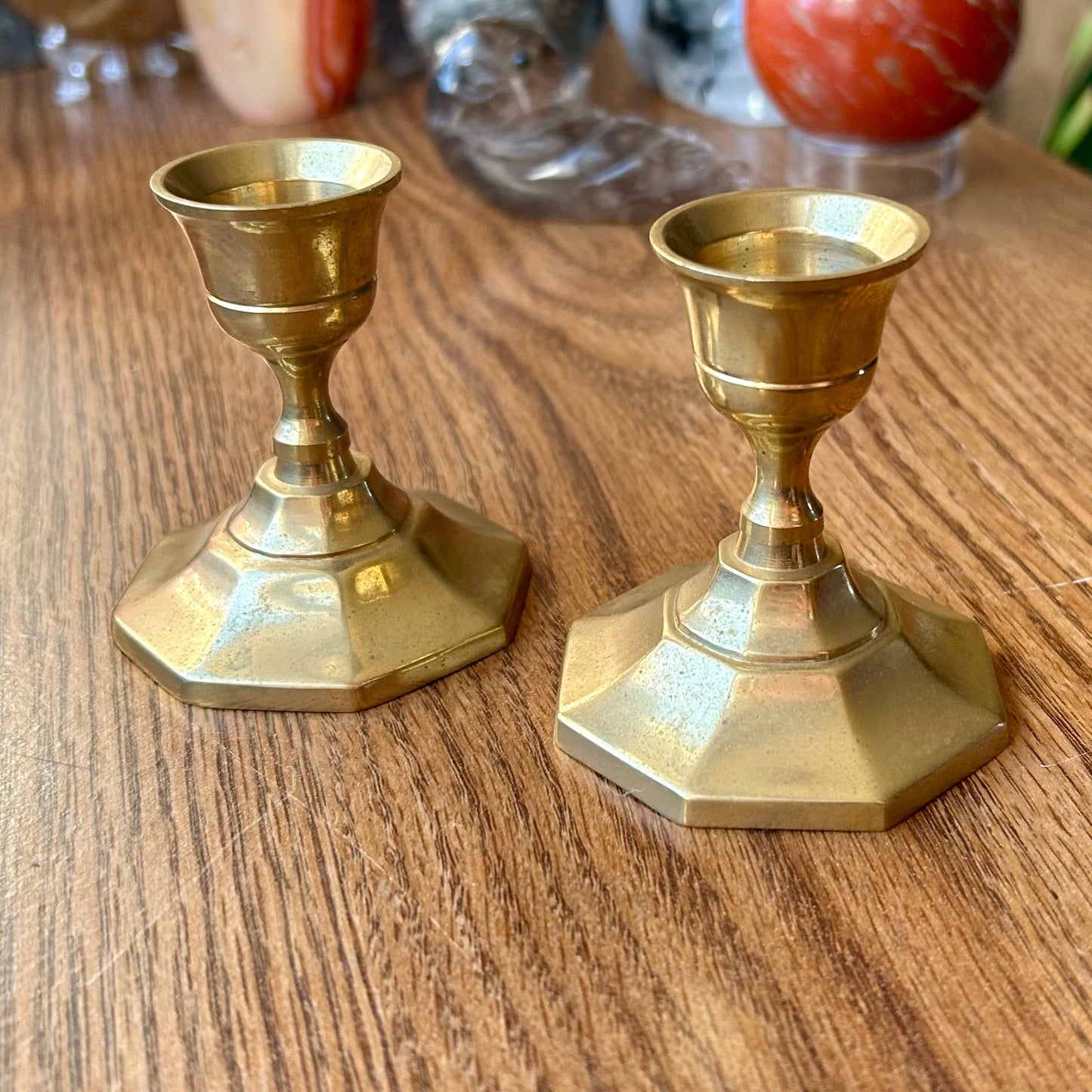 Two brass hexagonal candle holders on a wooden surface with decorative stones in the background.