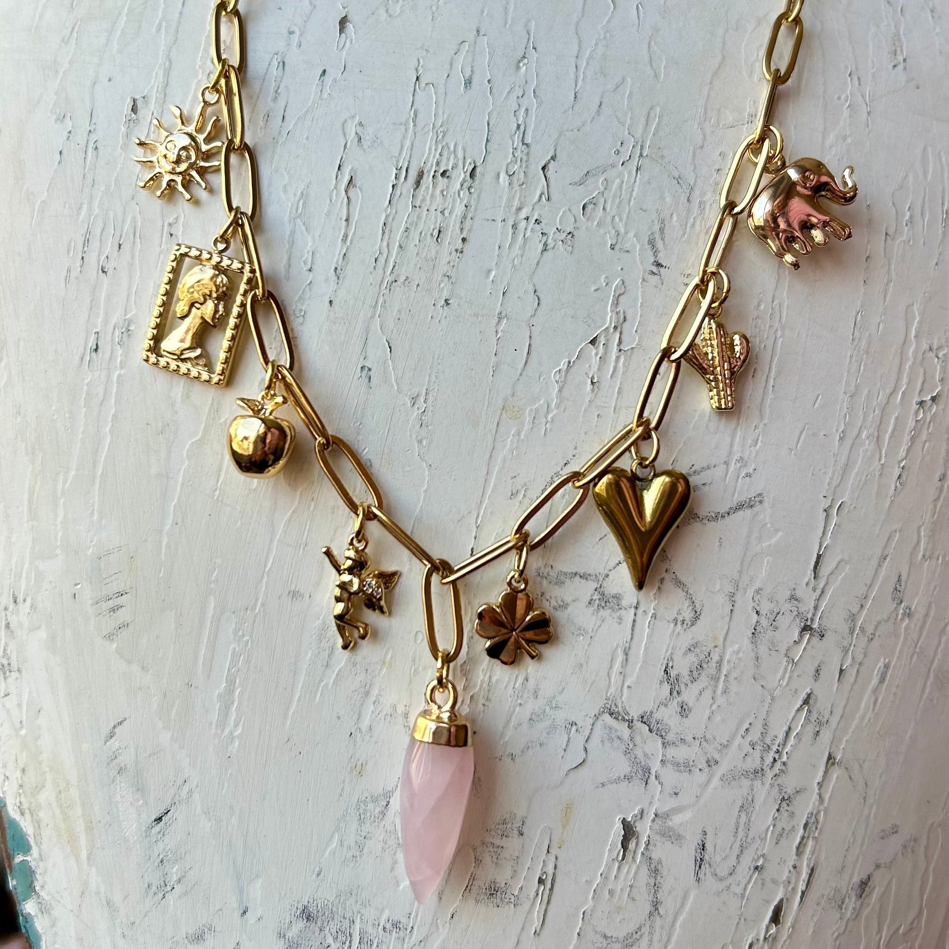 Gold necklace with various charms on a mannequin bust.