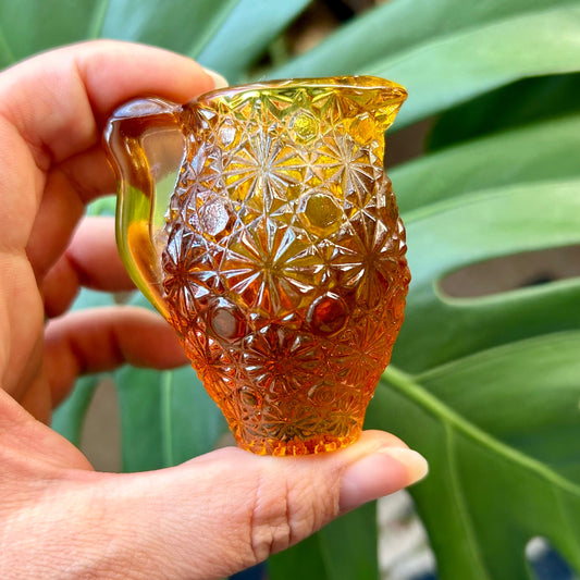 Hand holding a textured amber glass vase against a green leafy background