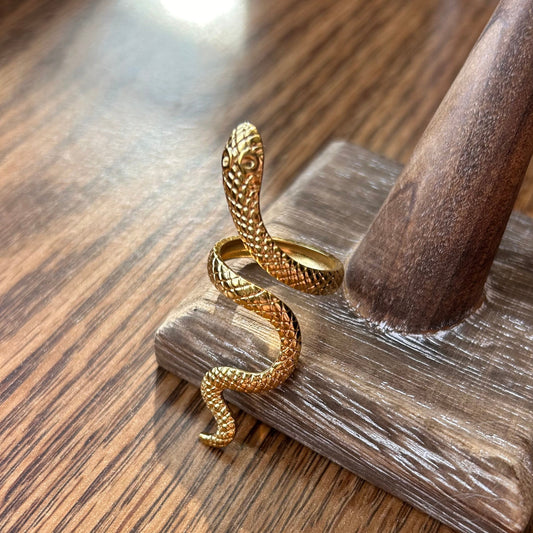 Gold snake-shaped ring on a wooden stand with a wooden surface background