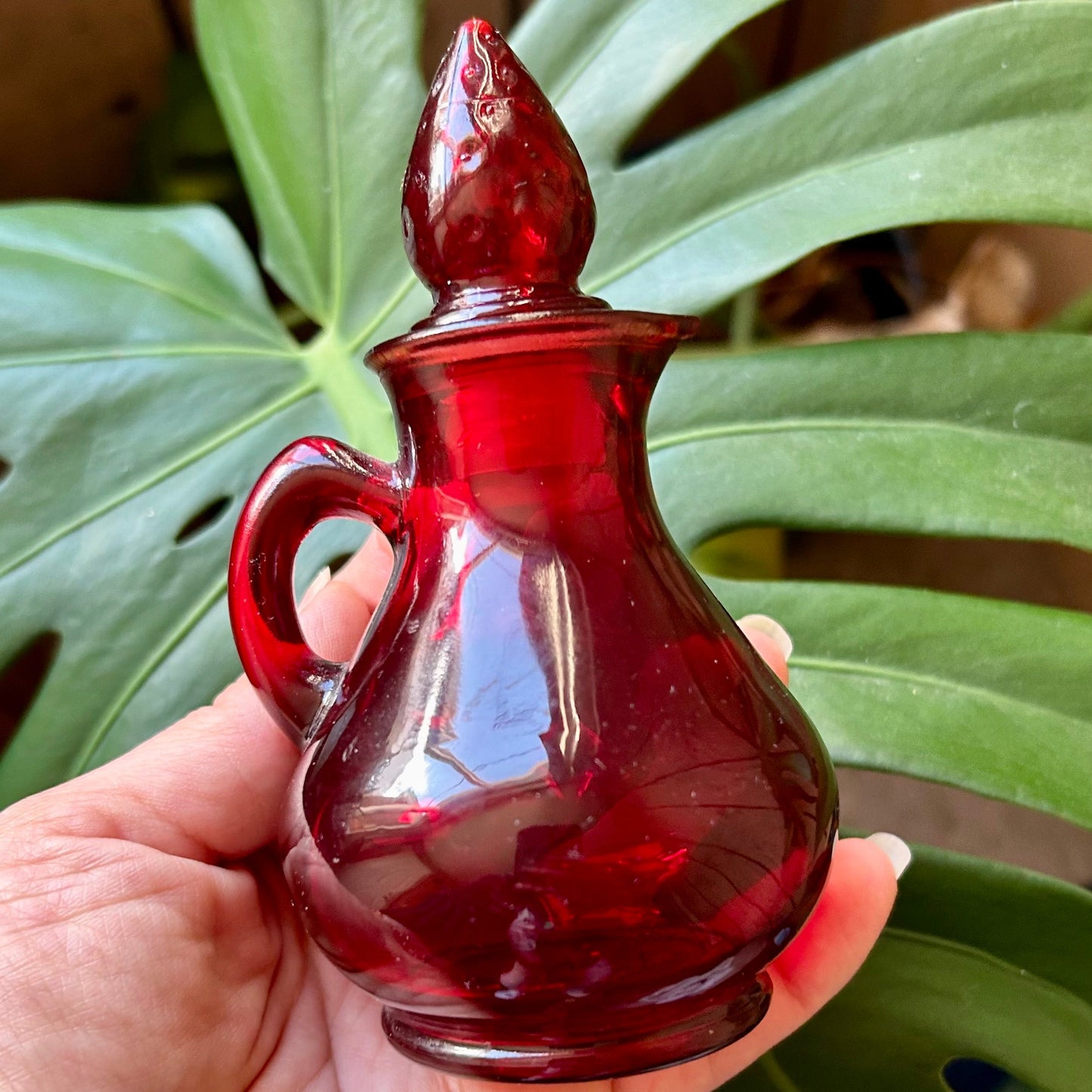 Red glass bottle held in a hand with green leaves in the background