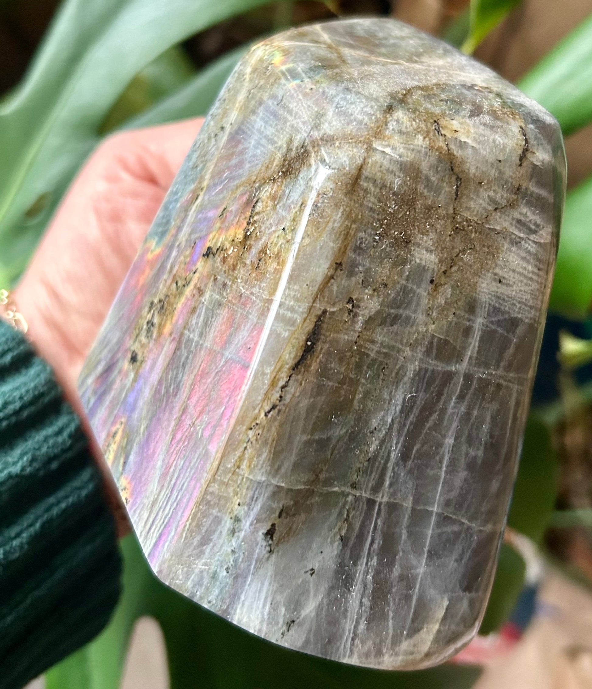 Polished crystal held by a hand with a blurred natural background