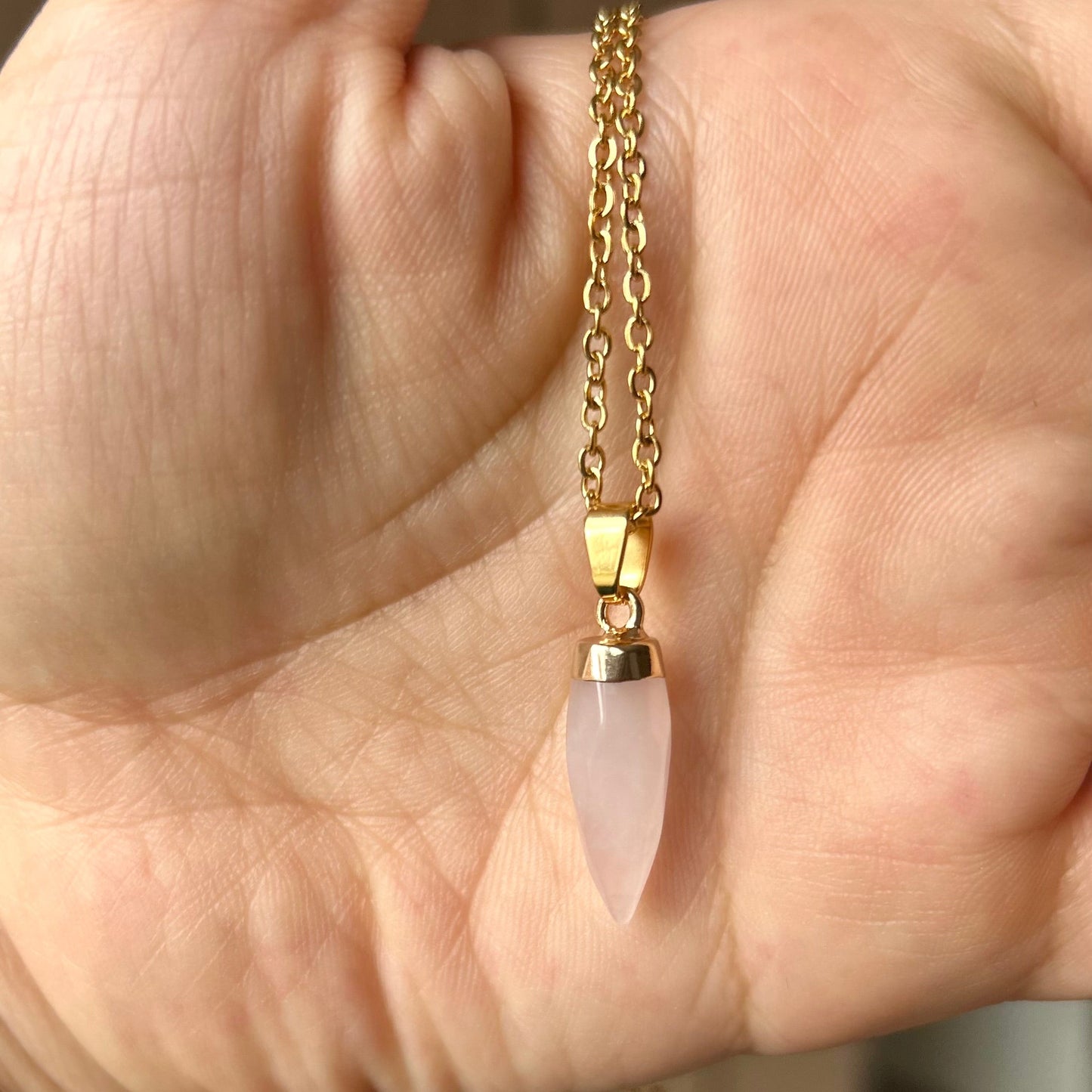 Gold chain necklace with a pink pendant held in a hand.