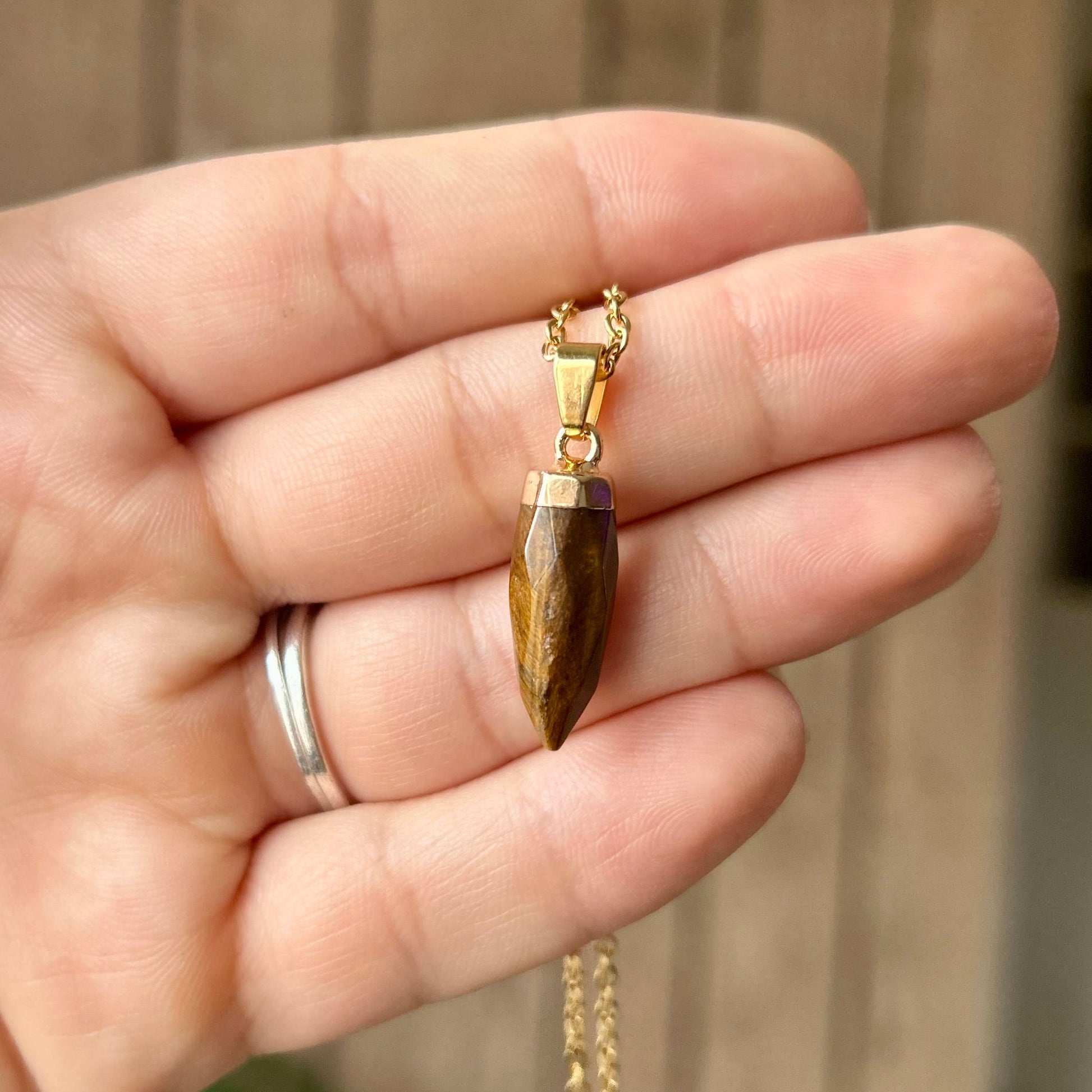 Hand holding a gold necklace with a pendant against a neutral background