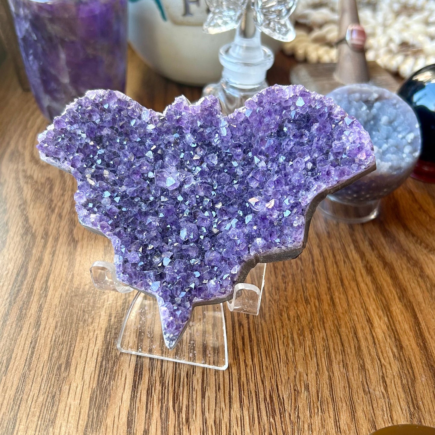 Purple crystal heart on a stand with a small butterfly figurine on a wooden surface.
