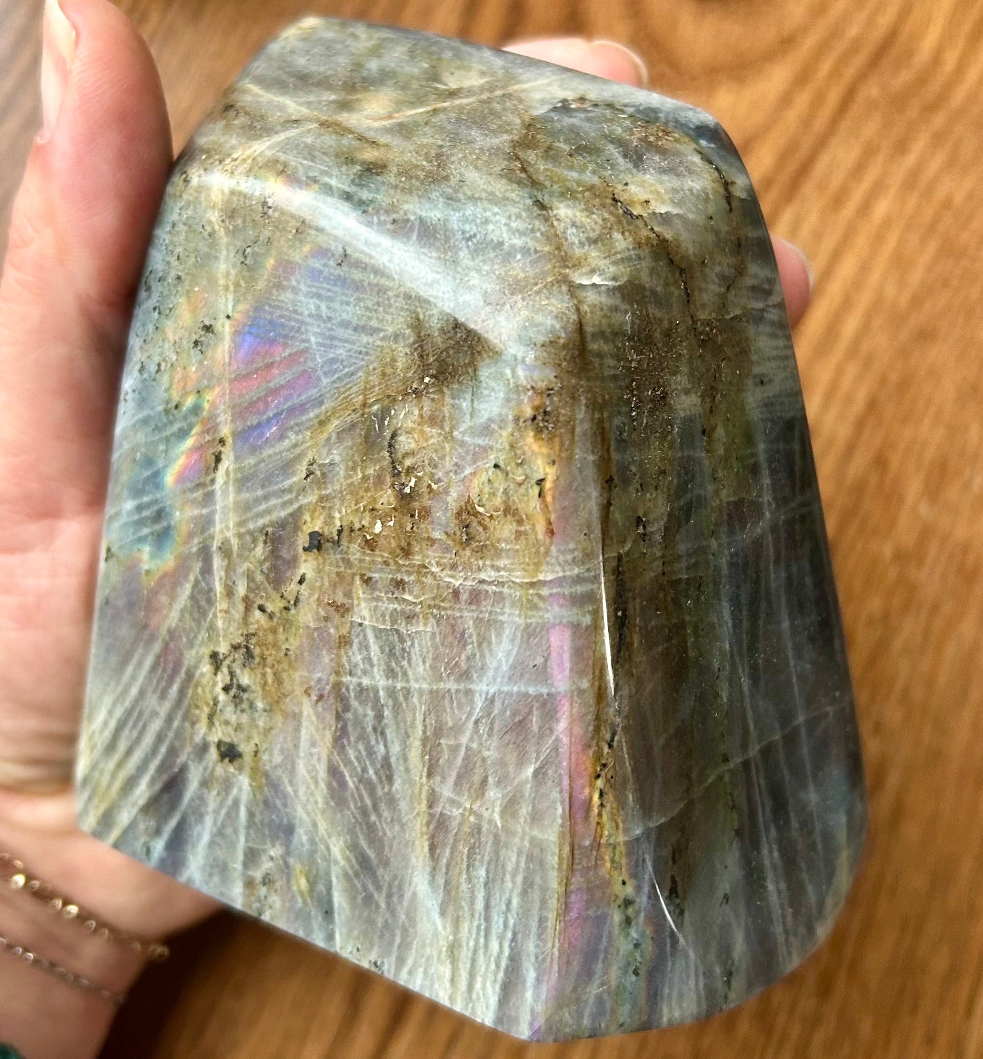 Hand holding a large crystal with colorful patterns on a wooden surface