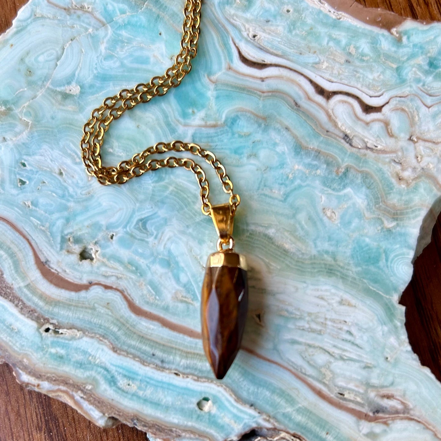 Gold necklace with a brown pendant on a decorative stone surface