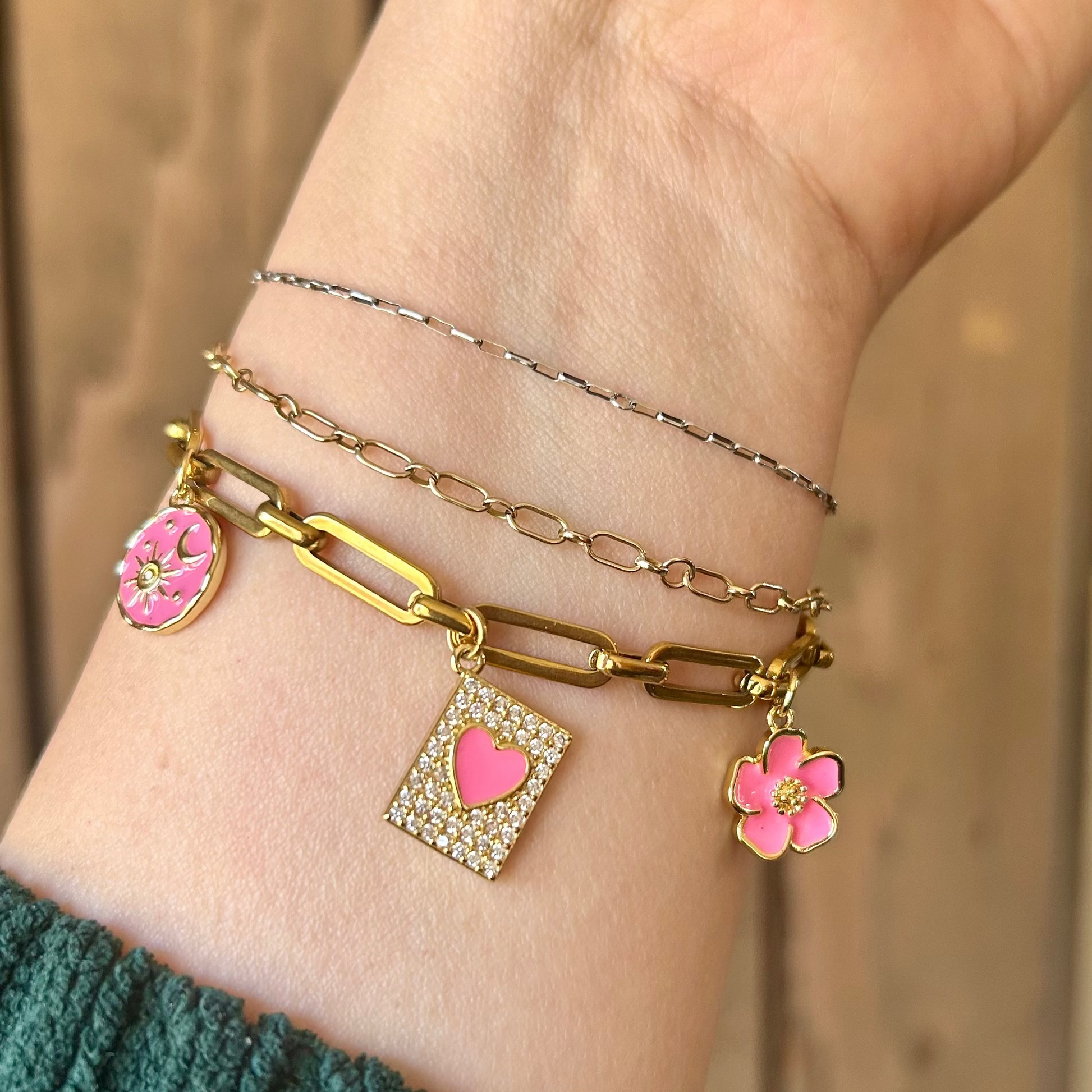 Hand wearing multiple bracelets with floral and heart charms on a wooden background